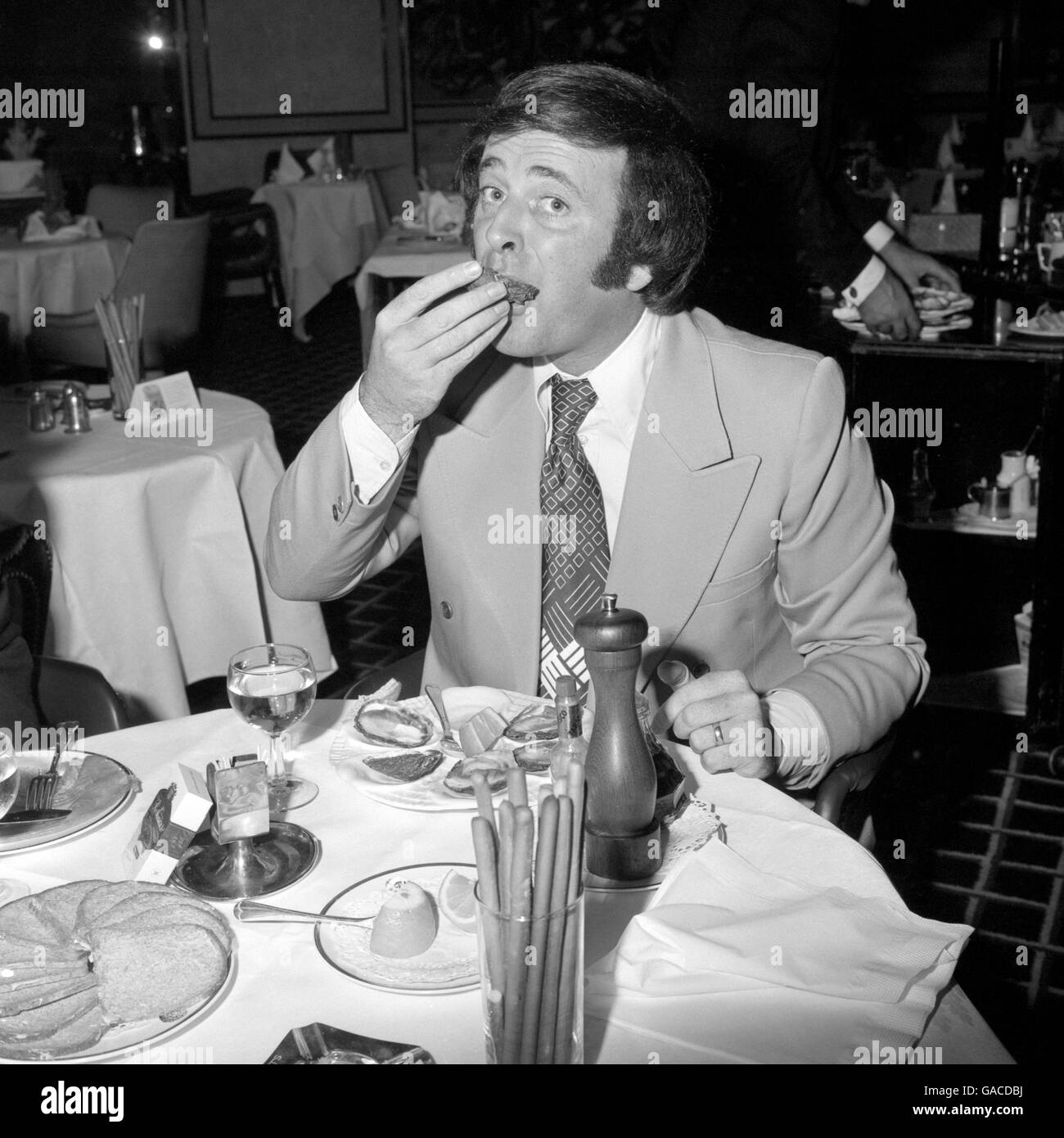 Personalità televisiva e radiofonica Terry Wogan assaggi un ostriche ad un ricevimento per celebrare l'apertura della stagione di ostriche 1973 al ristorante Scott's a Mount Street. Foto Stock