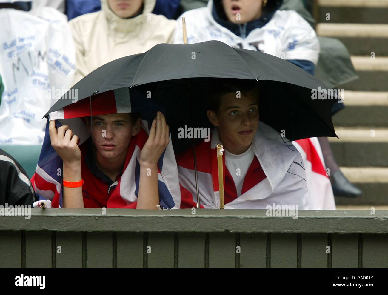 Due giovani ragazzi ricovero sotto il loro ombrello sperando di vedere Un po' di tennis mentre la pioggia cade sul Centro campo Foto Stock
