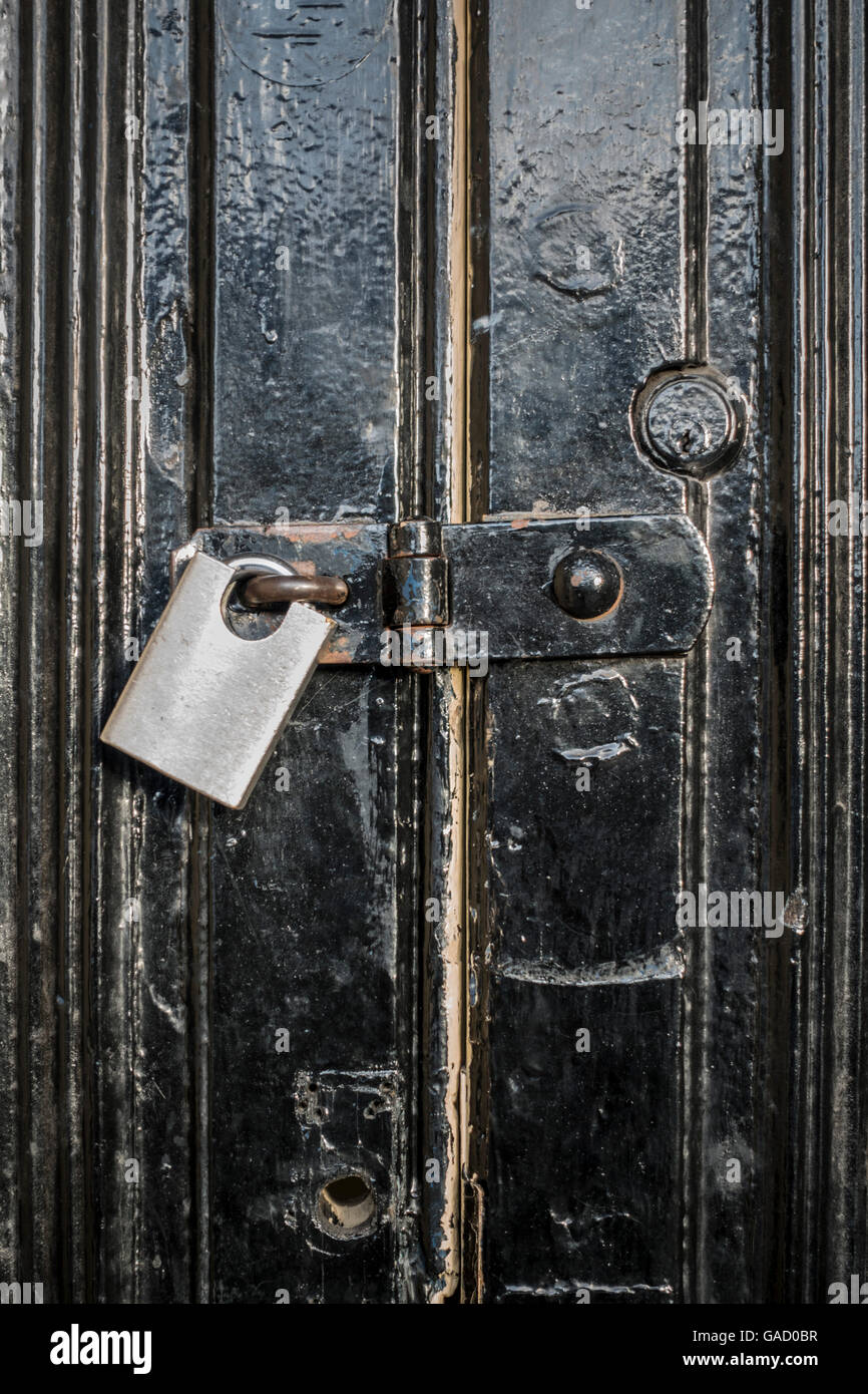 Un moderno lucchetto in acciaio inox su hasp di una coppia di molto vecchio nero porte verniciate Foto Stock