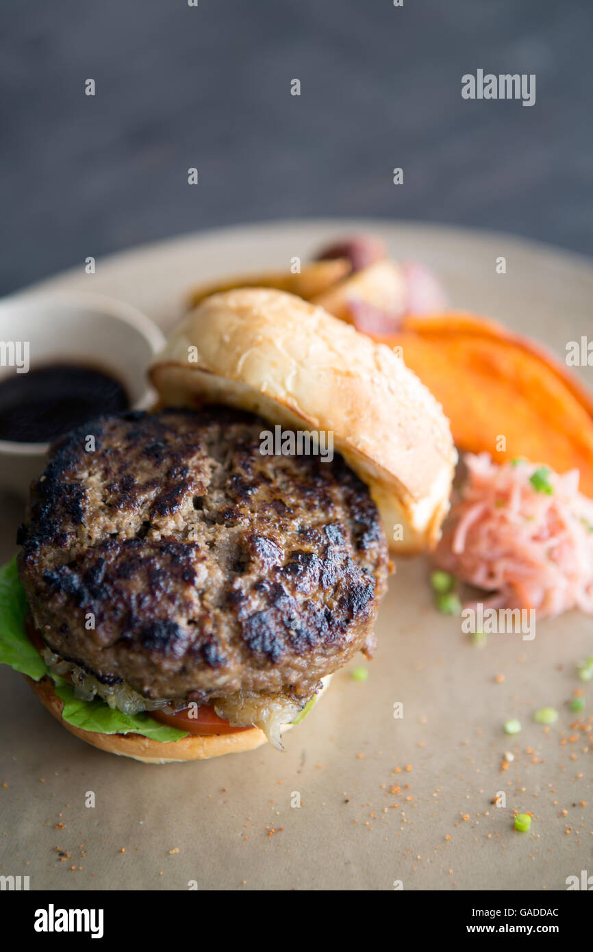 Un hamburger sano, di alta qualità, magro in pane fatto in casa servito con patate dolci patatine fritte e zeppe di patate, senza persone, primo piano, sfondo neutro Foto Stock