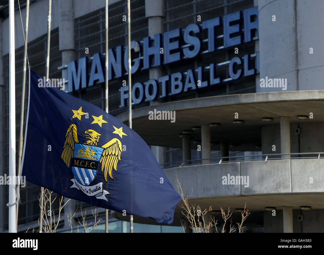 Bandiere fuori dal City of Manchester Stadium, sede del Manchester City FC, volano a metà albero. Oggi ricorre il 50° anniversario del disastro aereo di Monaco nel quale sono morti 8 giocatori del Manchester United. Foto Stock