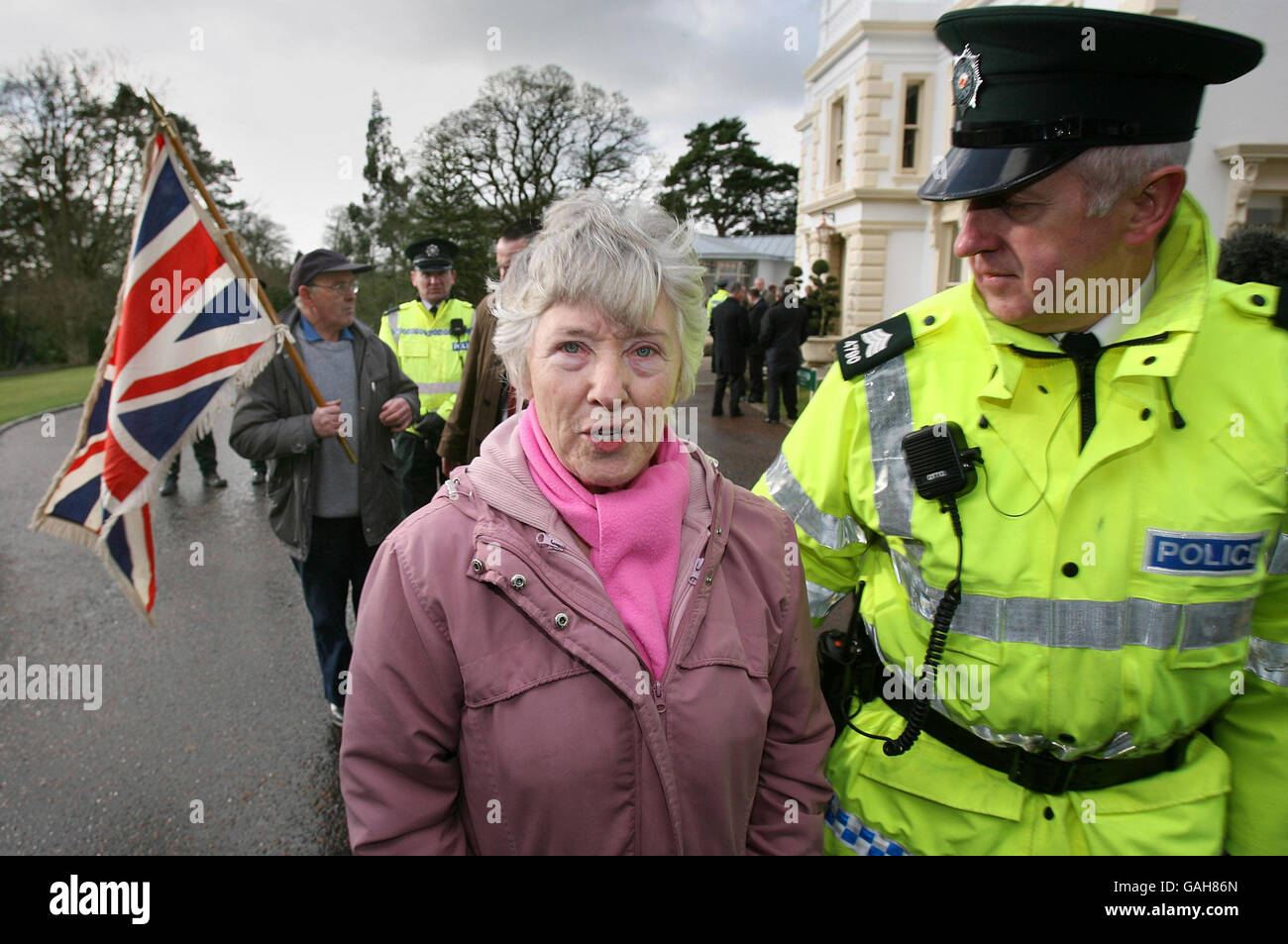Ruby Gillespie e il marito Roy (con bandiera) sono scortati dalla polizia del Galgorn Resort and Spa dopo aver protestato alla visita dell'irlandese Taoiseach Bertie Ahern e del primo ministro dell'Irlanda del Nord Ian Paisley. Foto Stock