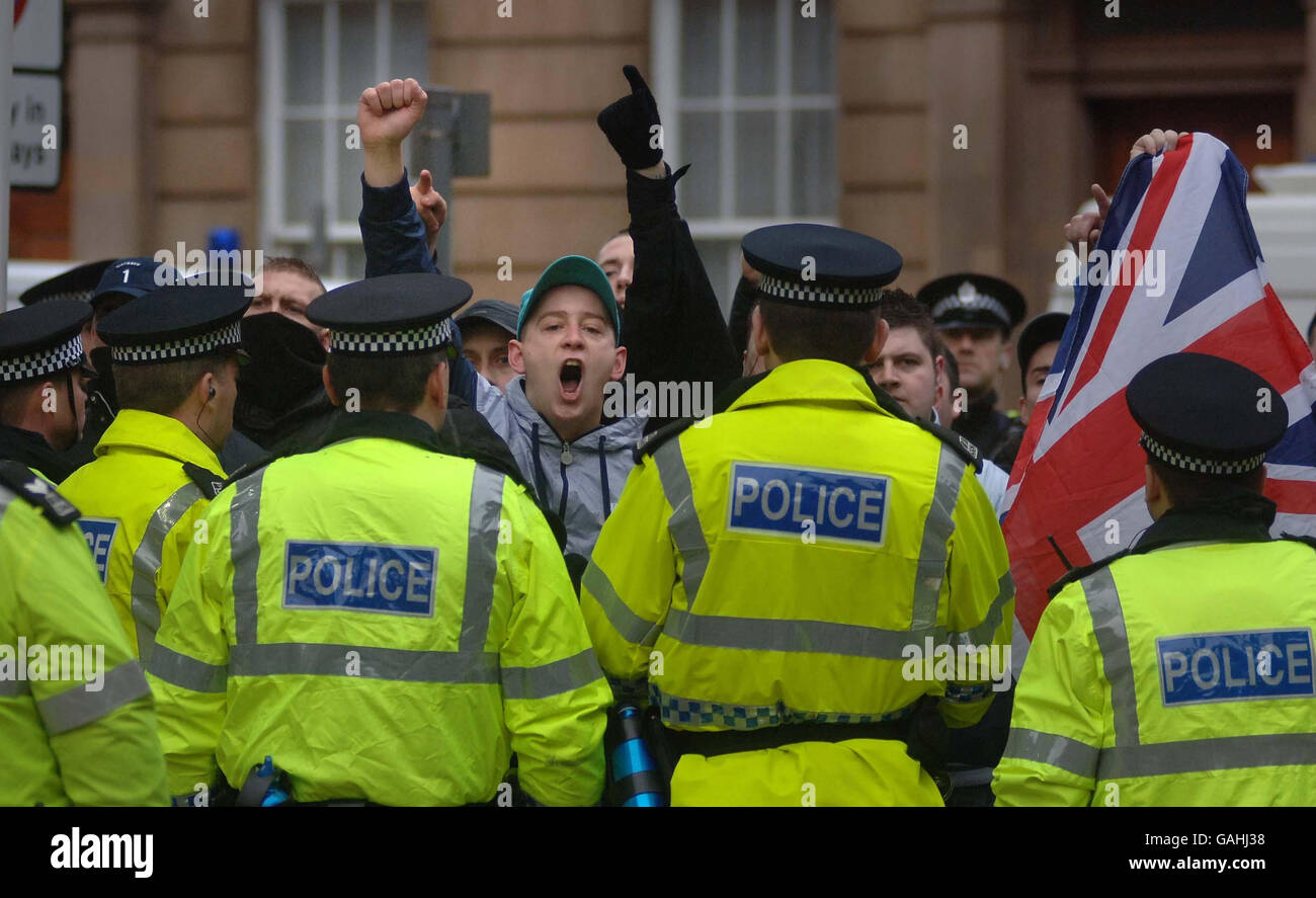 I manifestanti gridano e si lamentano dietro file di ufficiali di polizia in una parata per ricordare le vittime di Bloody Domenica a Glasgow questa mattina. Foto Stock