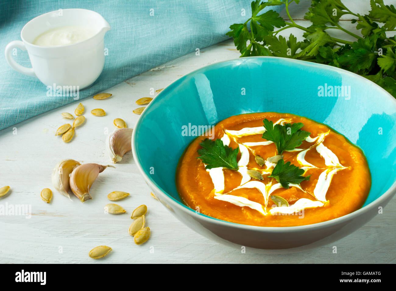 Zucca zucca vegetale zuppa cremosa e rabboccato con la crema di latte in una piastra di turchese, semi di zucca, aglio e prezzemolo su legno bianco b Foto Stock