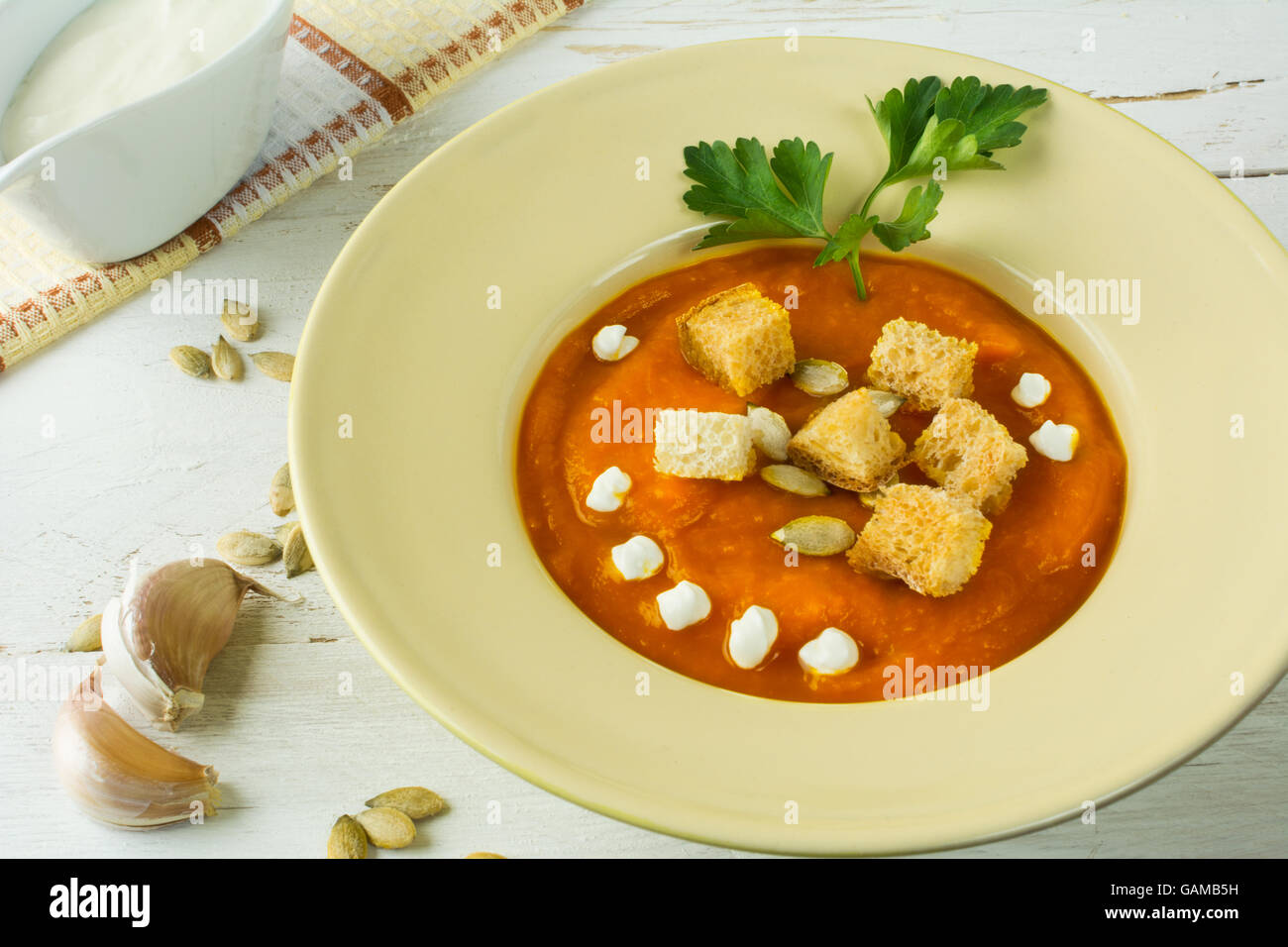 Zucca zucca minestra di verdura con crema, semi di zucca, crostini di aglio e prezzemolo in una luce gialla sul piatto di legno bianco bac Foto Stock