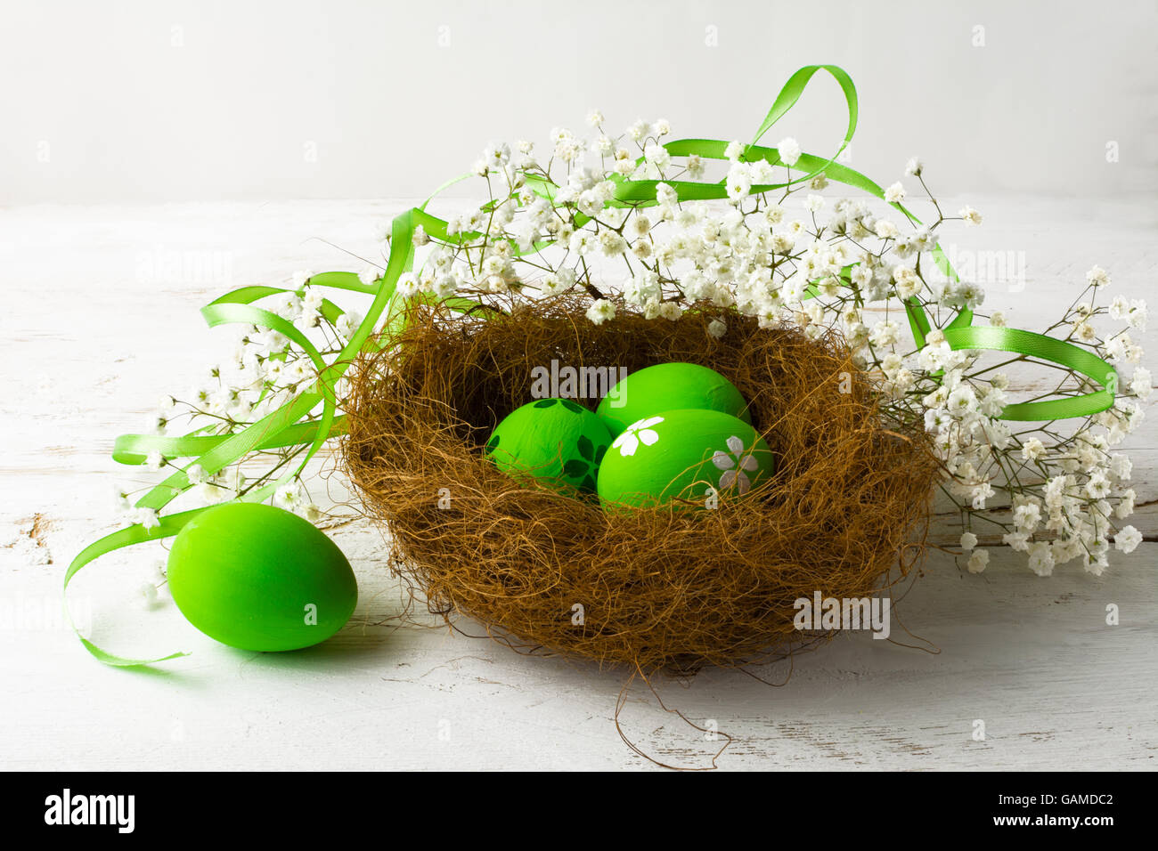 Verde di uova di Pasqua in un nido verde con nastro di raso su un bianco sullo sfondo di legno Foto Stock