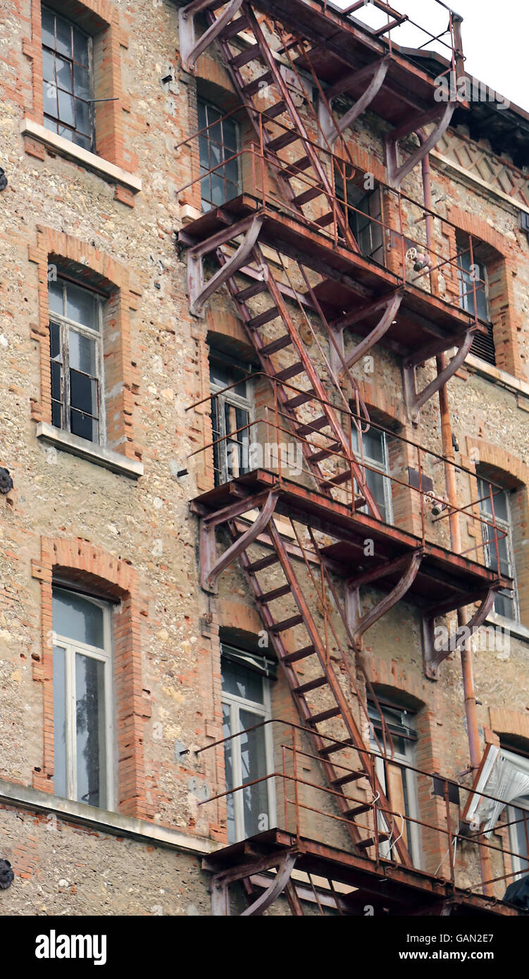 Fatiscente edificio industriale con rusty via di fuga in caso di incendi e di rottura vetri Foto Stock
