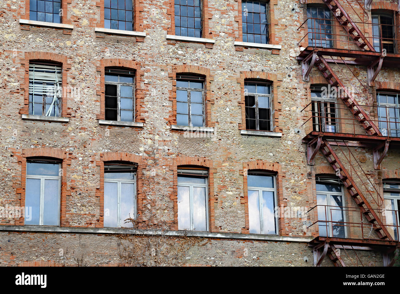 Fatiscente edificio industriale con fire escape con mattoni a vista e le finestre rotte Foto Stock