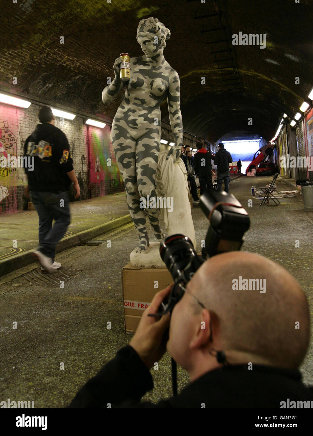 Un fotografo ispeziona una statua dell'artista di graffiti Banksy (chiamata 'periodo di Brew') al 'festival delle lattine' in un tunnel stradale in Leake Street, Lambeth, Londra. Foto Stock