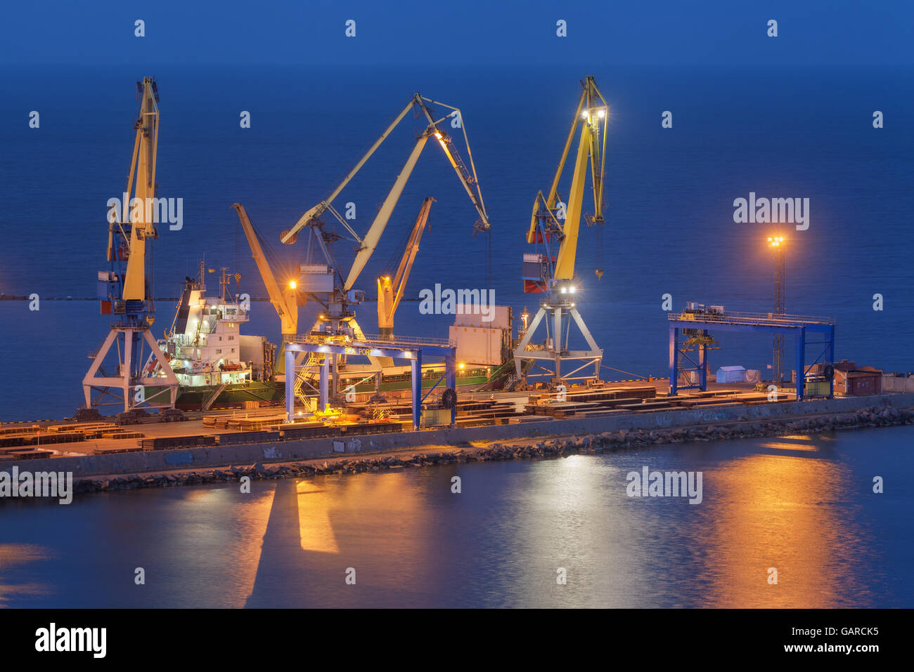 Merci spedite con gru di lavoro bridge nel porto di mare al crepuscolo. Porto commerciale di notte in Mariupol, Ucraina. Indust Foto Stock