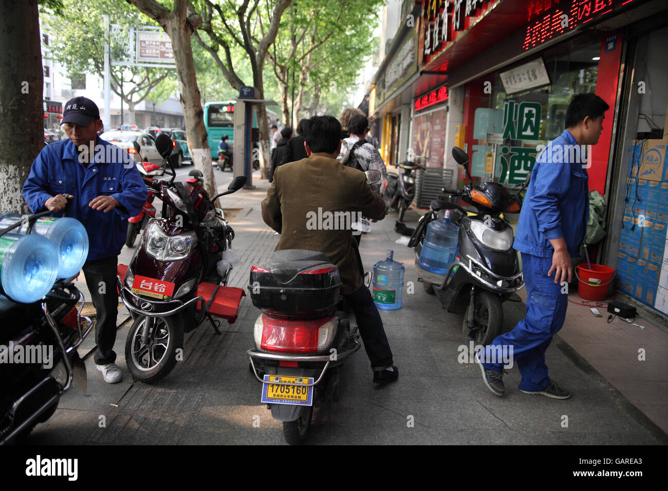 Un uomo cinese è tipicamente in sella al suo scooter sul marciapiede, egli è la manovra molto veloce tra gli altri scooter e pedoni. Suzhou, Cina. Foto Stock