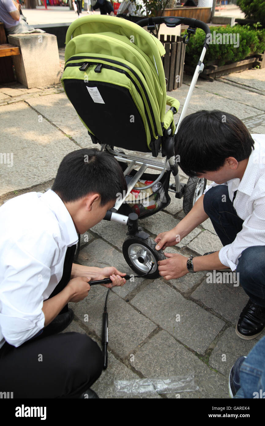 Giovane uomo pompa aria manualmente in una ruota di un passeggino, il suo amico controlla la ruota, sono turisti nel mezzo di visite turistiche. Tongli, Cina. Foto Stock