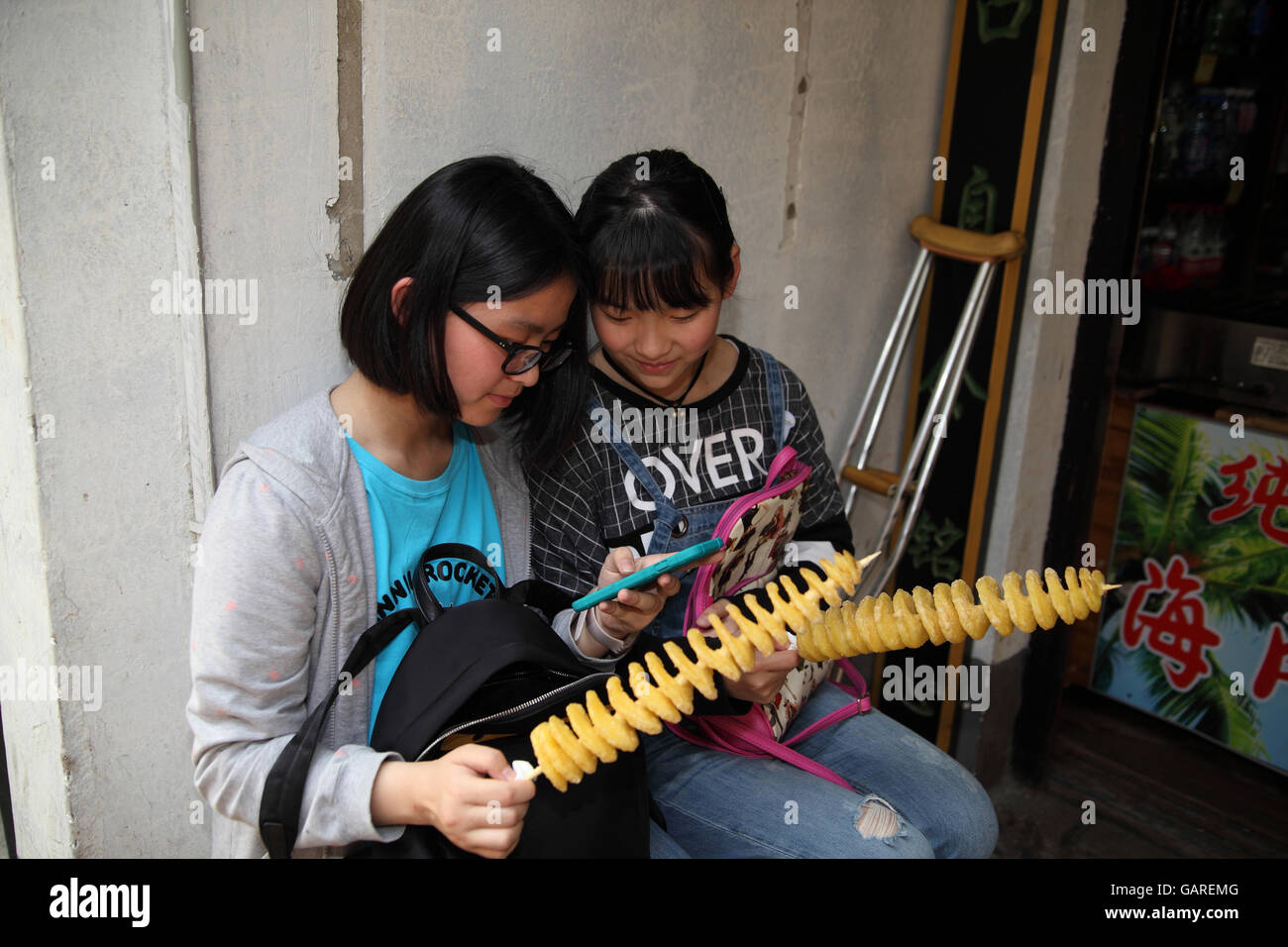 Due ragazze cinesi siedono insieme con la caramella nelle loro mani, essi sono la visione di un video su uno smartphone appartenente ad uno di essi. Tongli , Cina. Foto Stock