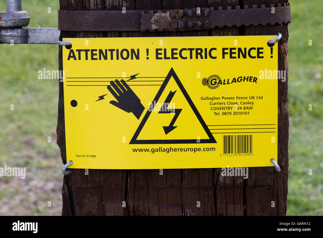 Un segno di avvertimento e recinto elettrico che circonda un campo di pecore "ATTENZIONE! Recinto elettrico! Foto Stock