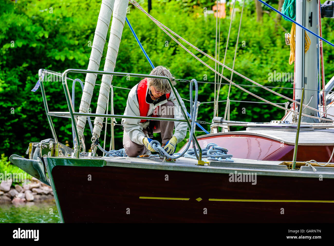 Motala, Svezia - 21 Giugno 2016: Senior donna legatura di un nodo sulla prua di una barca a vela di colore marrone. La vita reale situazione. Foto Stock