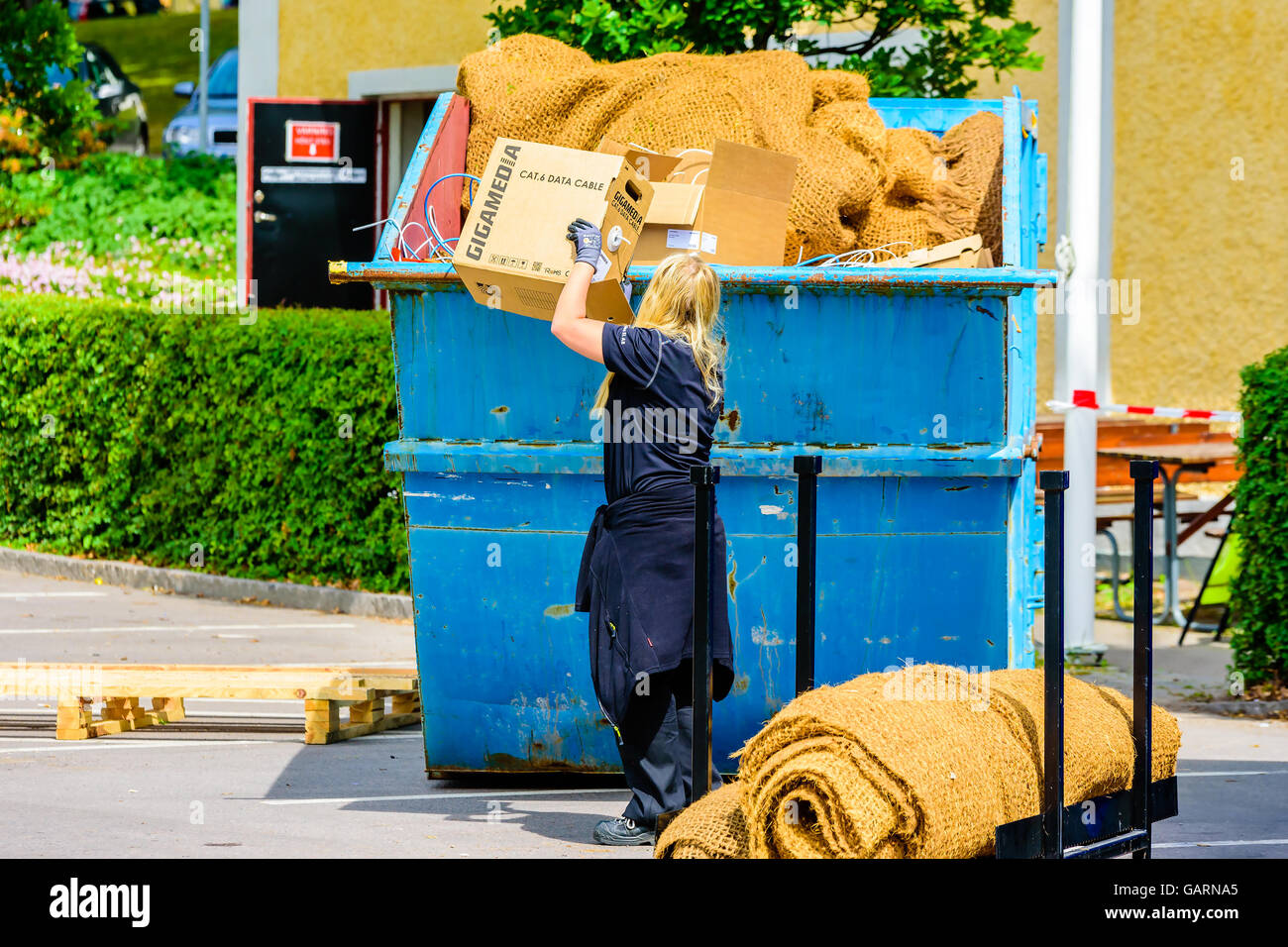 Motala, Svezia - 21 Giugno 2016: giovane donna adulta gettando via una cassetta di carta con il cavo dati in un contenitore di rifiuti. Lif reale Foto Stock