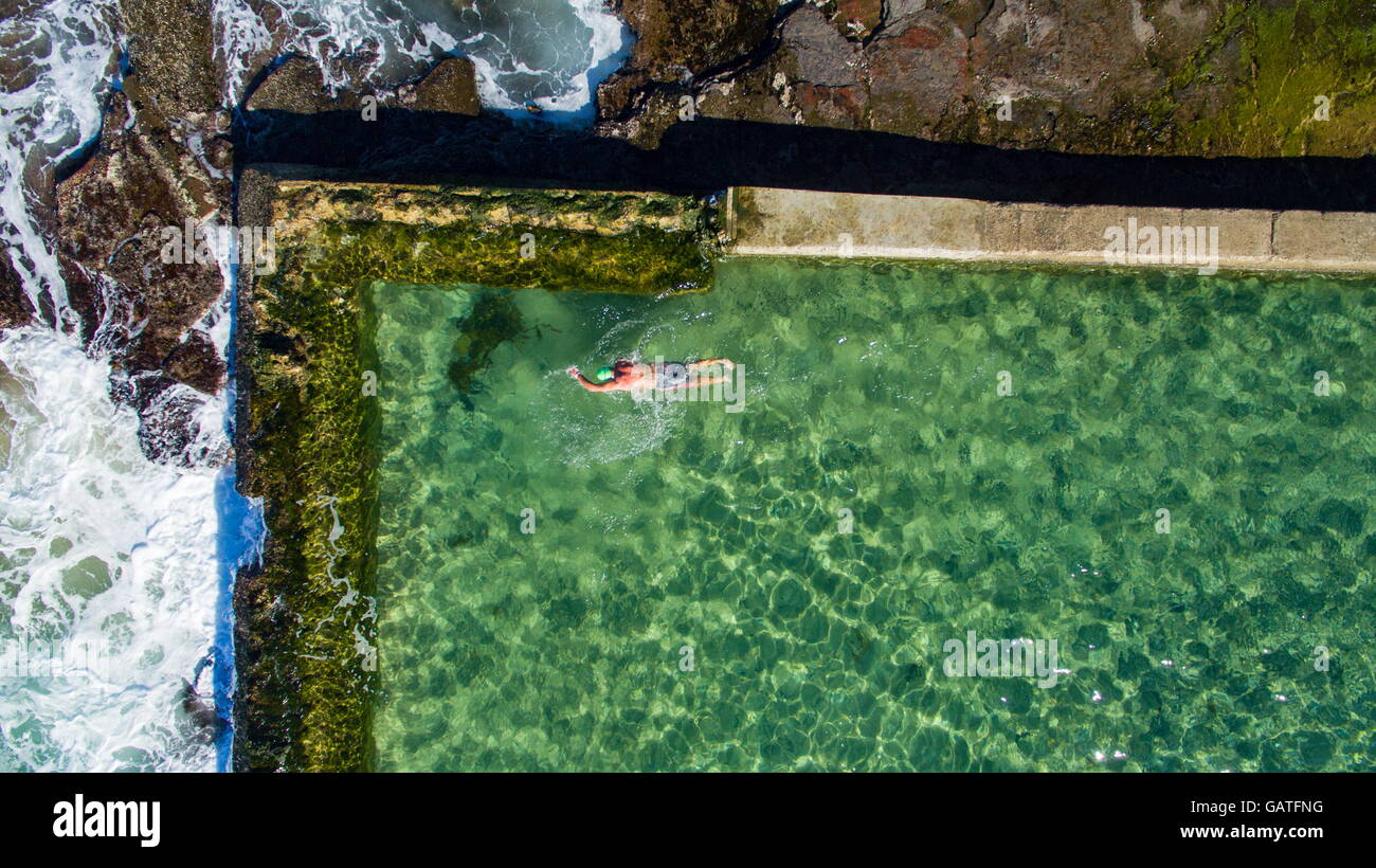 Un nuotatore solitario nuota giri nell'oceano Austinmer rock pools, visto dall'alto. Foto Stock