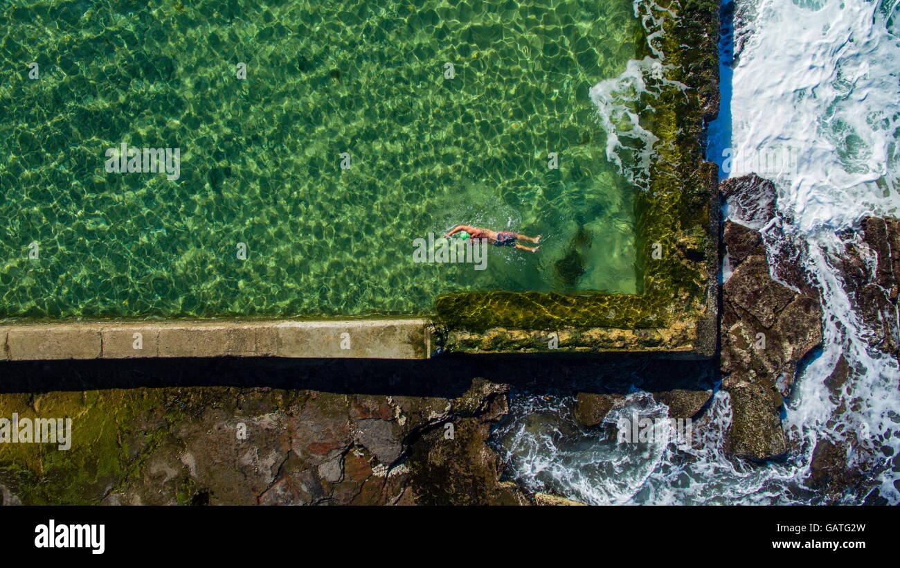 Un nuotatore solitario nuota giri nell'oceano Austinmer rock pools, visto dall'alto. Foto Stock