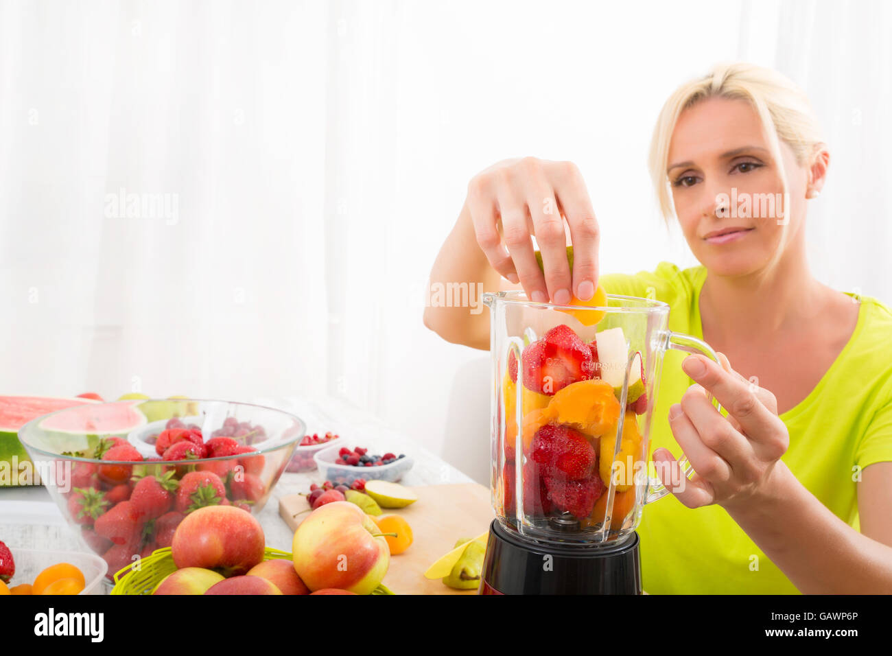 Una bella donna matura preparare un frullato o succo di frutta in cucina. Foto Stock