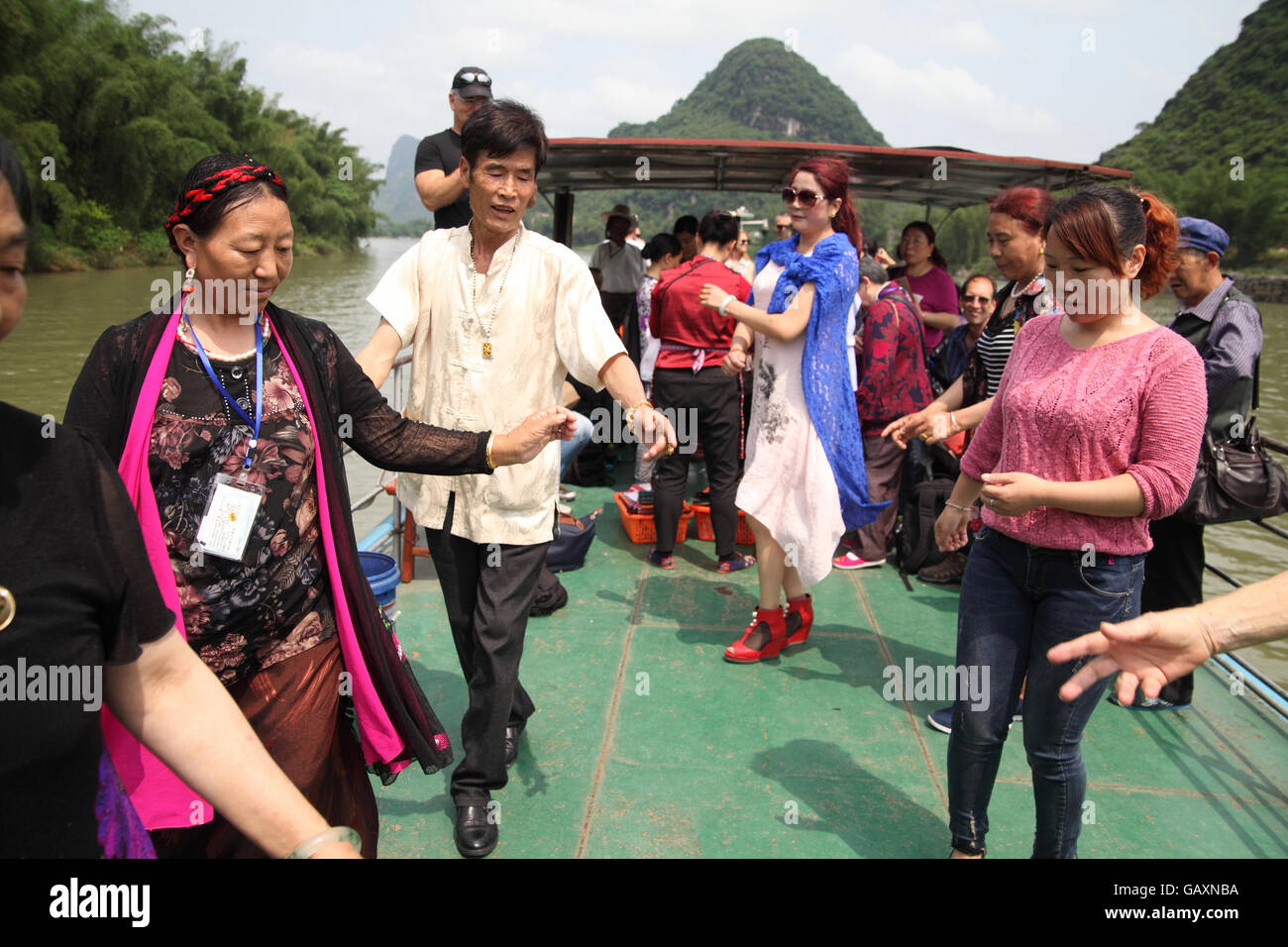 Persone di una famiglia tibetana, turisti, danza una danza tibetana su una nave da crociera con altri turisti in giro. Il fiume Li vicino Yangtshuo, Cina Foto Stock