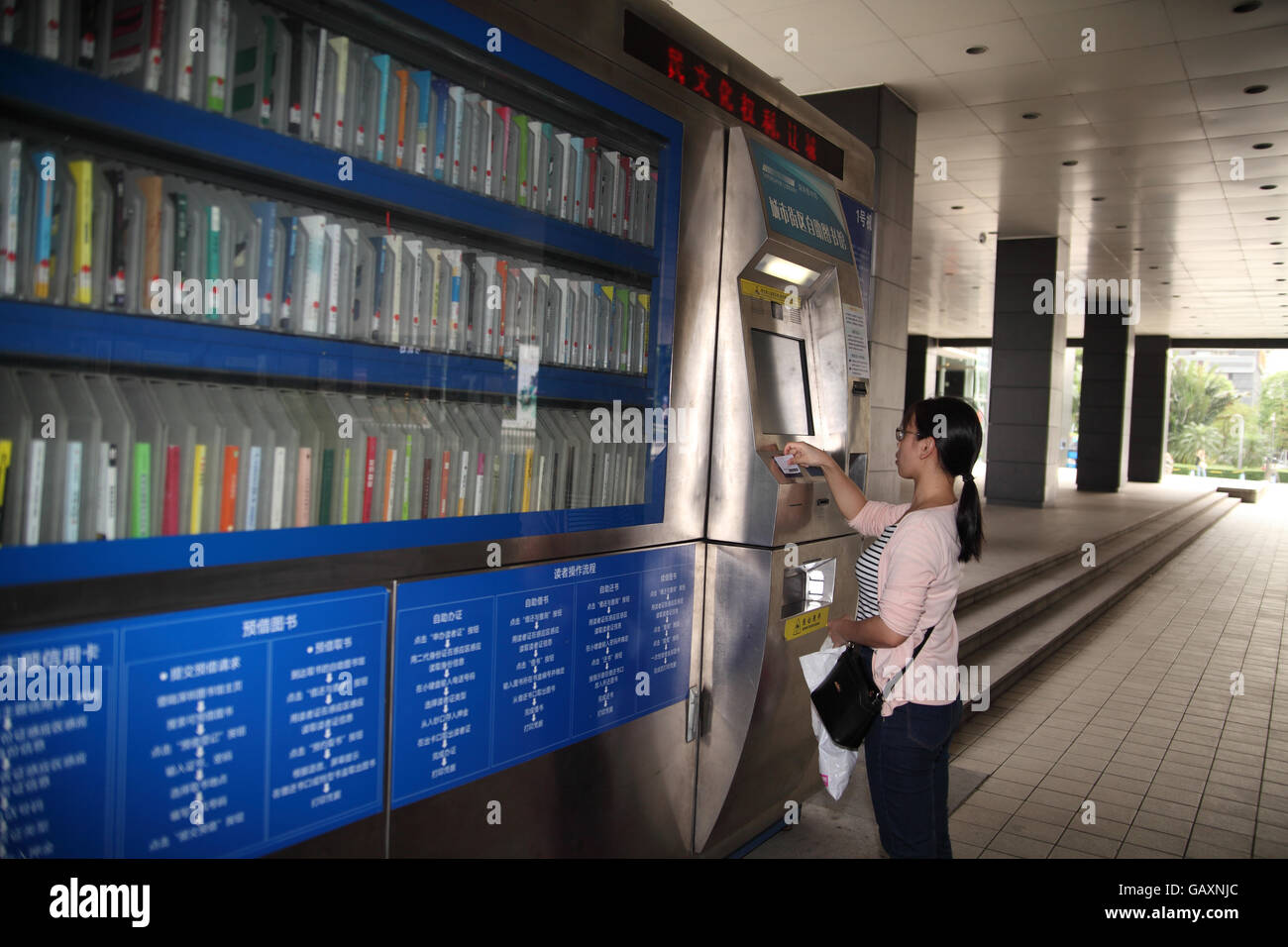 Una giovane donna Chine utilizzando un sistema automatico di self service library macchina da affittare o prendere in prestito un libro. Shenzhen, Cina Foto Stock