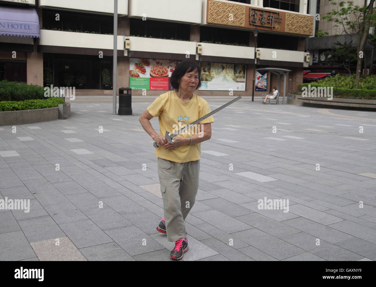 Un anziano pensionato donna cinese è molto intensly concentrando utilizzando una spada come lei fa Tai Chi in un parco pubblico utilizzando una lancia. Kowloon, Hong Kong. Foto Stock
