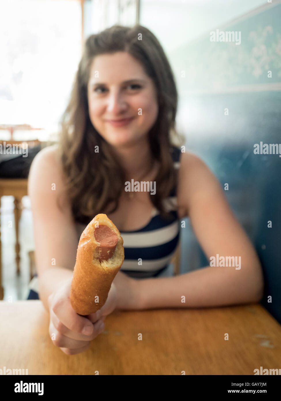 Una bella ragazza con un cane di mais (corndog). Messa a fuoco selettiva sul mais cane. *** Modello di rilascio disponibili su richiesta.*** Foto Stock