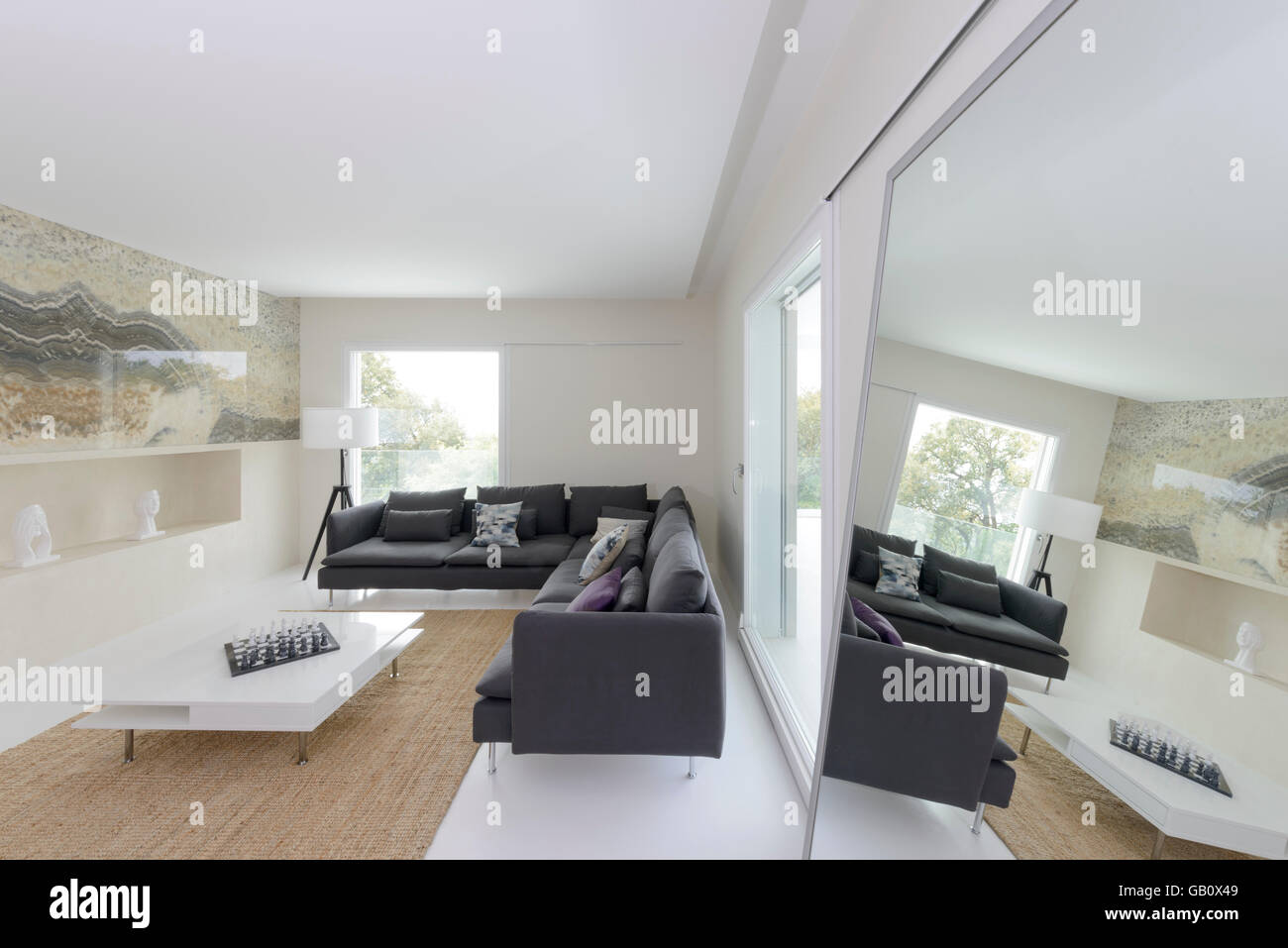Moderno soggiorno con specchio che riflette grandi divani e ampie finestre luminose Foto Stock