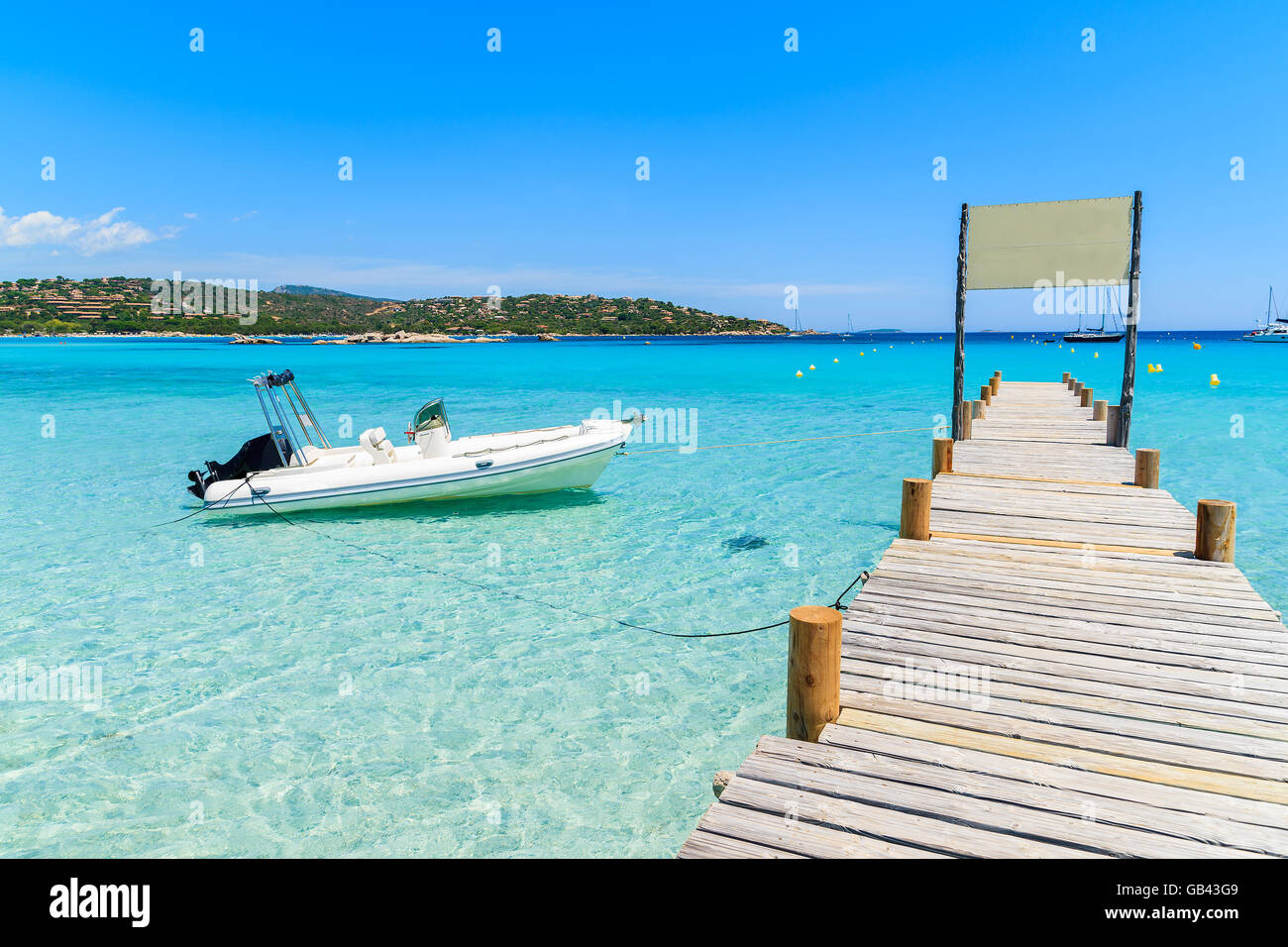Pontile in legno sulla spiaggia di Santa Giulia con gommone sul mare azzurro, Corsica, Francia Foto Stock