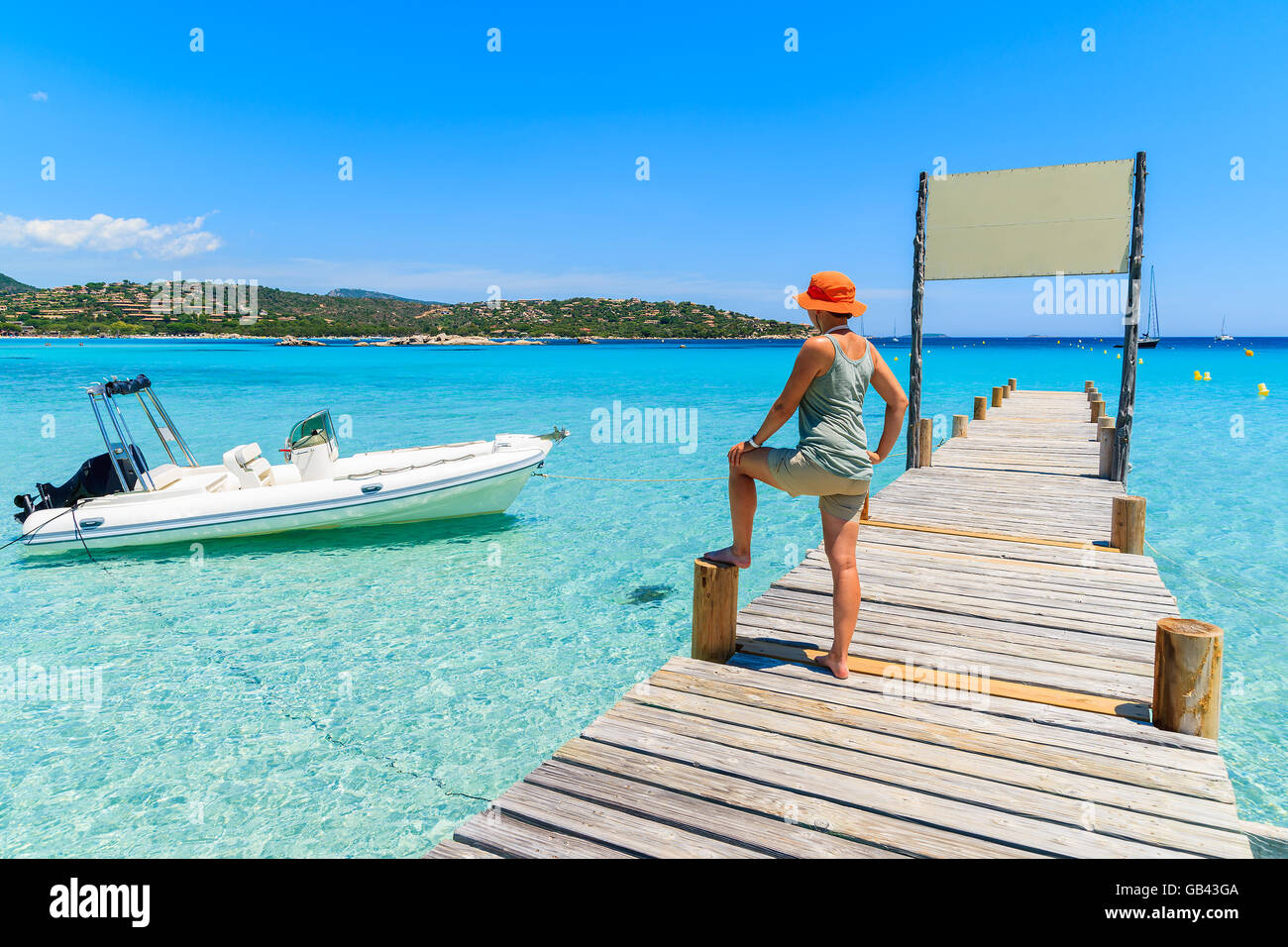 Giovane donna turista in piedi sul pontile in legno sulla spiaggia di Santa Giulia cercando in gommone sul mare azzurro, Corsica, Francia Foto Stock