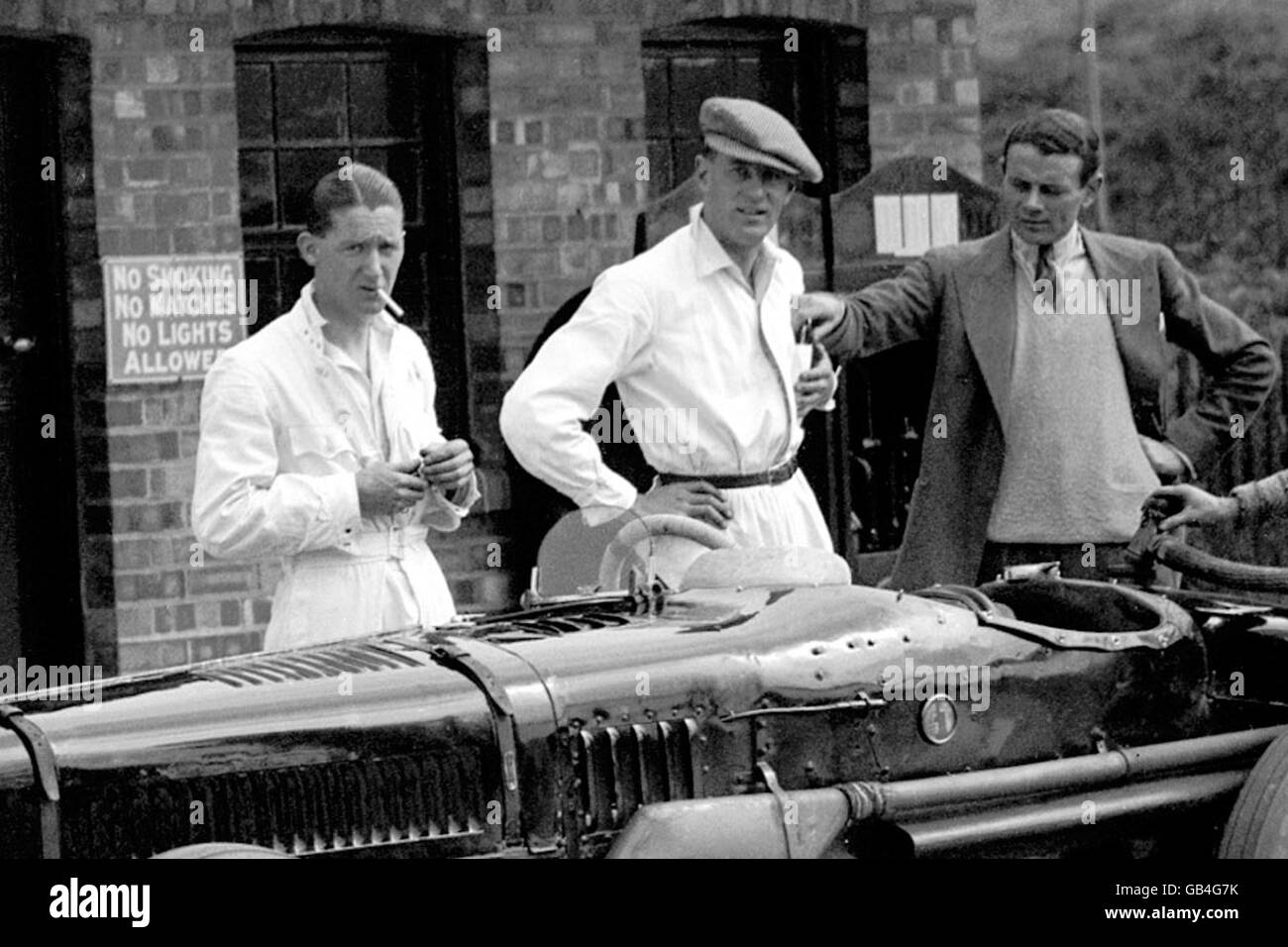 Motor Racing - distributore di benzina - Brooklands. Un meccanico del distributore di benzina Brooklands guarda con ansia il fotografo mentre si prepara sconsigliatamente ad accendere una sigaretta Foto Stock