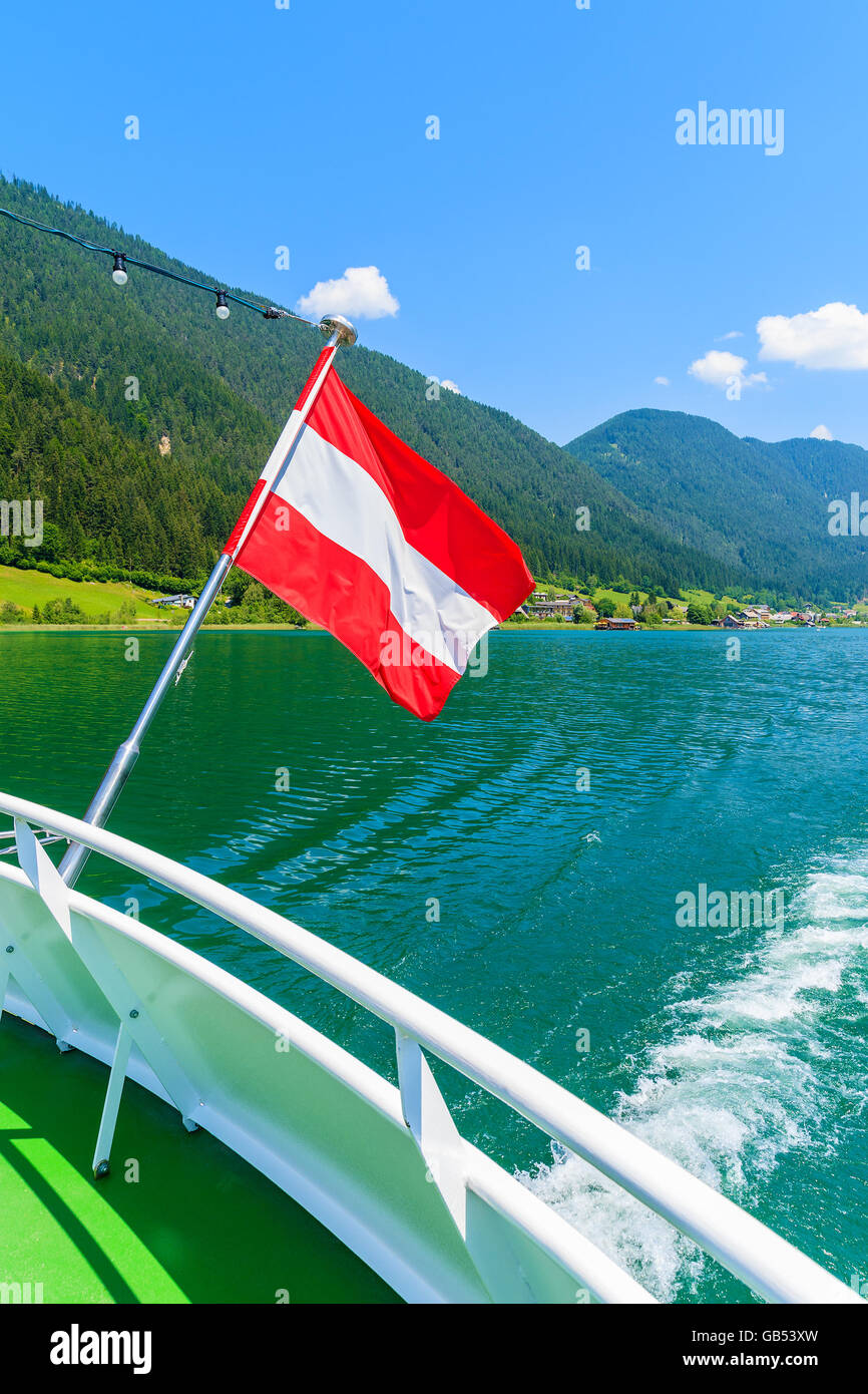 Bandiera austriaca sventolare sul vento durante la nave crociera su acqua verde lago Weissensee, Austria Foto Stock