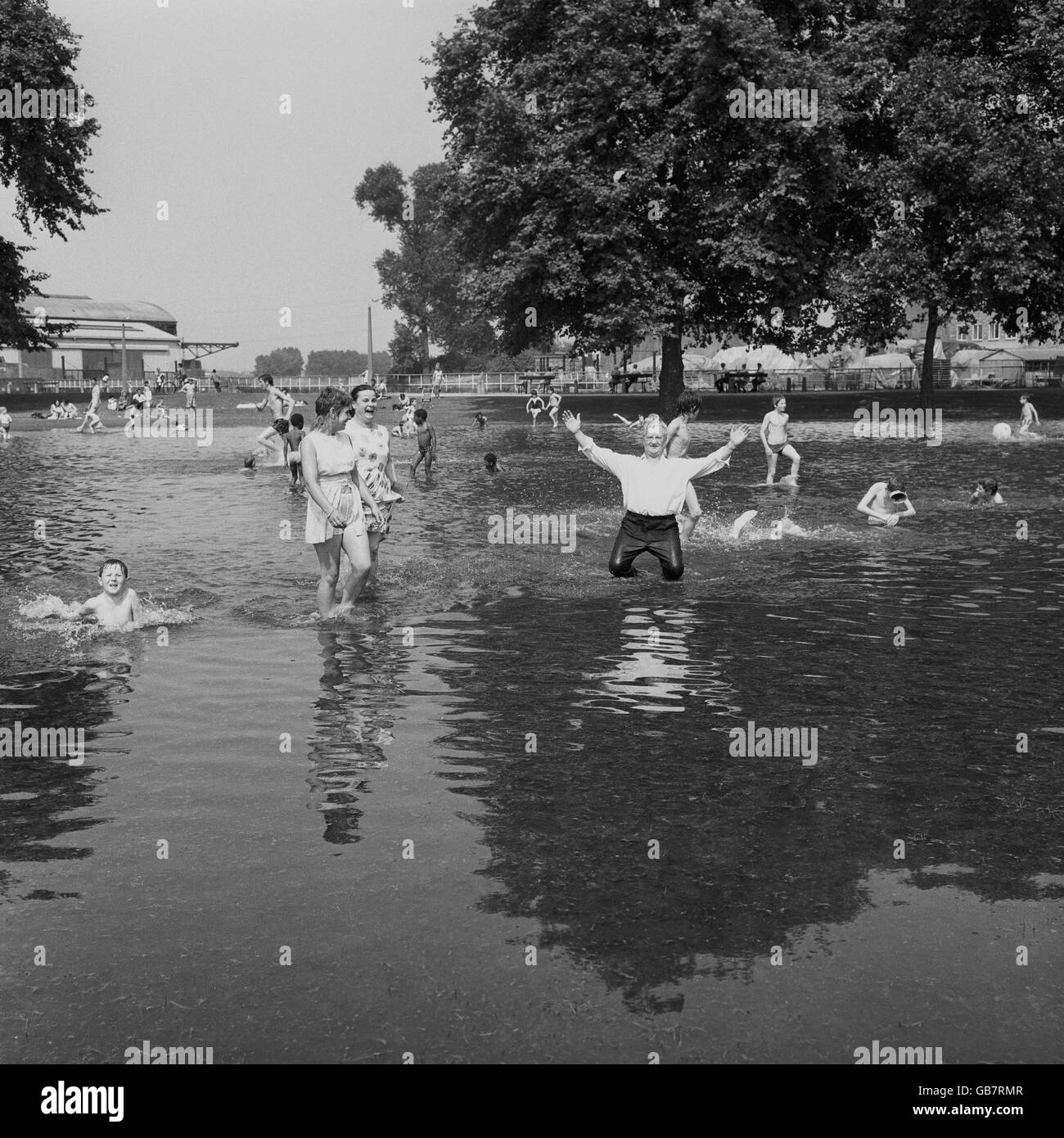 Wet-trousered MR F Lloyd, a destra, sua moglie Dora, seconda a sinistra, e Sylvia Dodd, a sinistra, vicini a Glyn Road, a est di Londra, Wade in acqua di alluvione per rinfrescare fuori dal caldo al campo di ricreazione di North Millfields. L'istante mare è venuto al loro quartiere dopo che una rete idrica scoppiò nelle vicinanze. Foto Stock