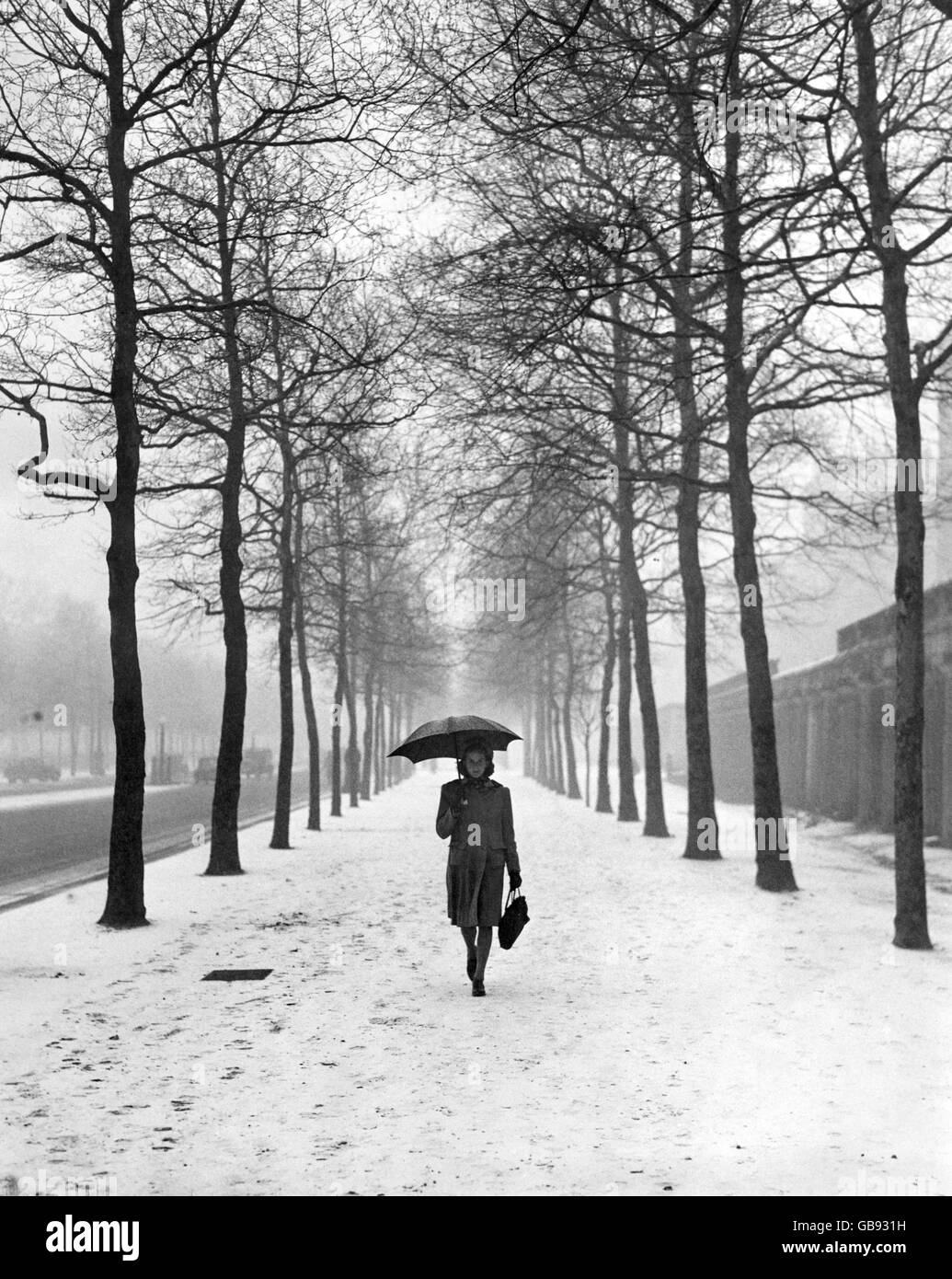 Un solitario camminatore nel centro commerciale che tiene il suo ombrello per proteggersi dalla neve. Foto Stock
