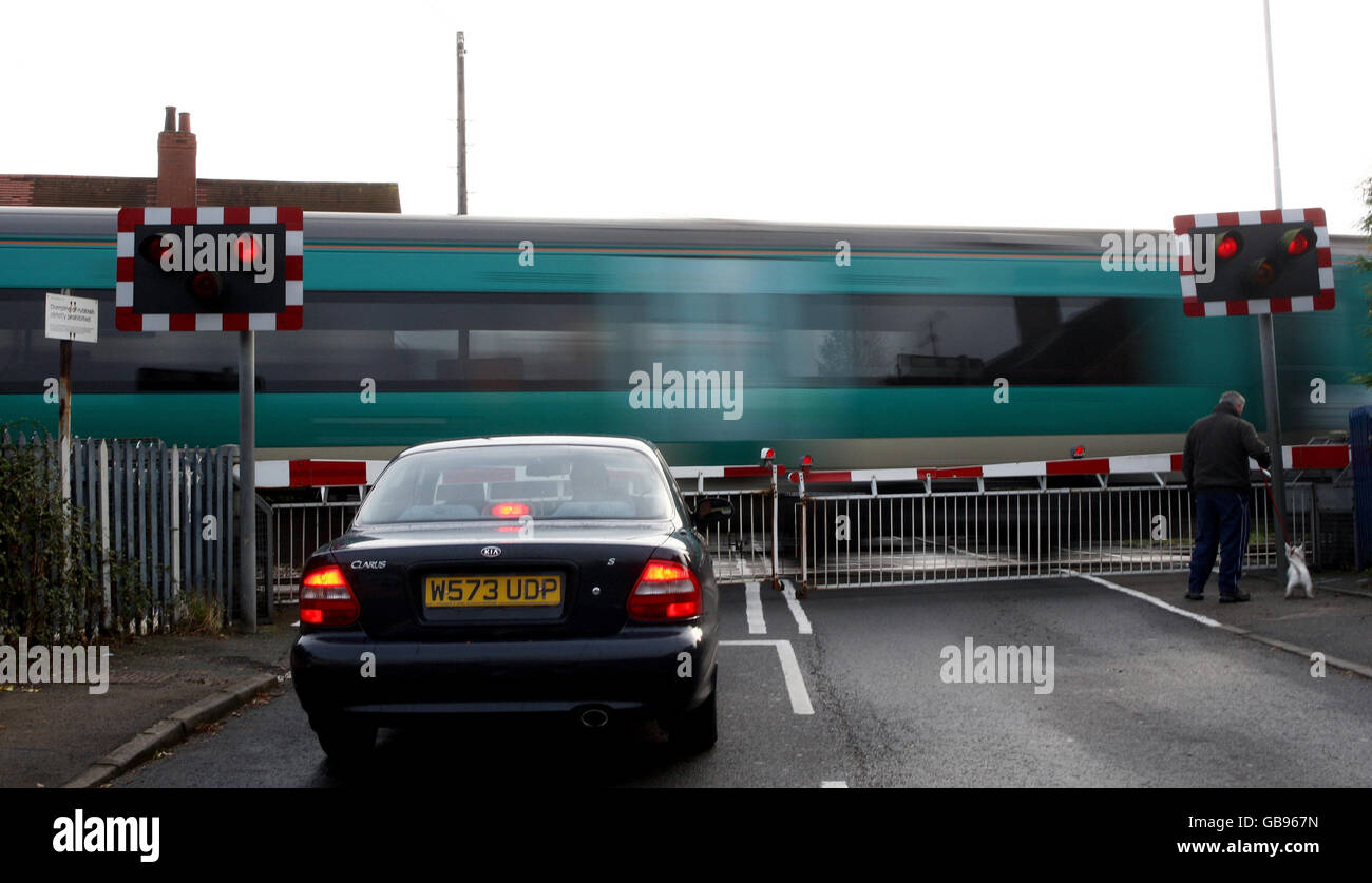 Un'auto e un pedone aspettano a un livello attraversando come un trio attraversa a Prestbury, Cheltenham, Gloucestershire. Foto Stock