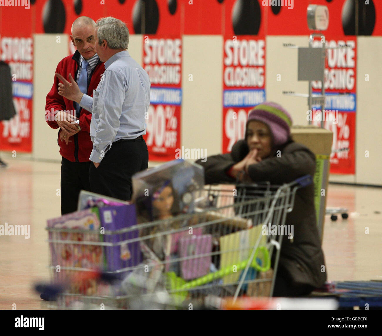 Un acquirente con un trolley imballato prende una pausa durante l'ultimo giorno di negoziazione presso il negozio Woolworths a Edimburgo, mentre i membri del personale parlano in background. Foto Stock