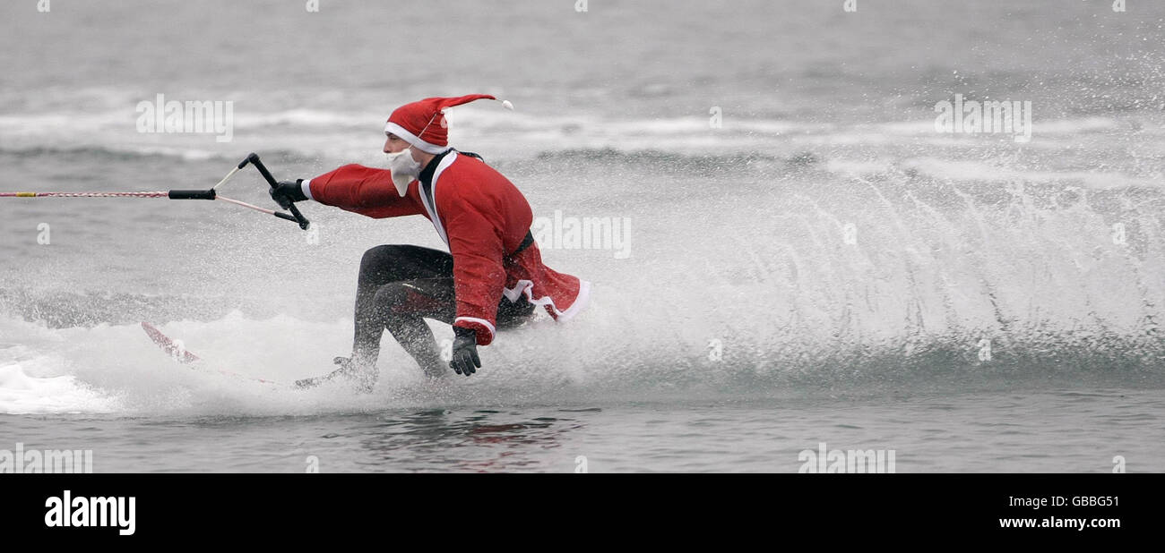 Un uomo vestito da sci d'acqua di Santa per l'intrattenimento di coloro che prendono parte alla nuotata annuale di Natale vicino Sandycove, Dublino. Foto Stock