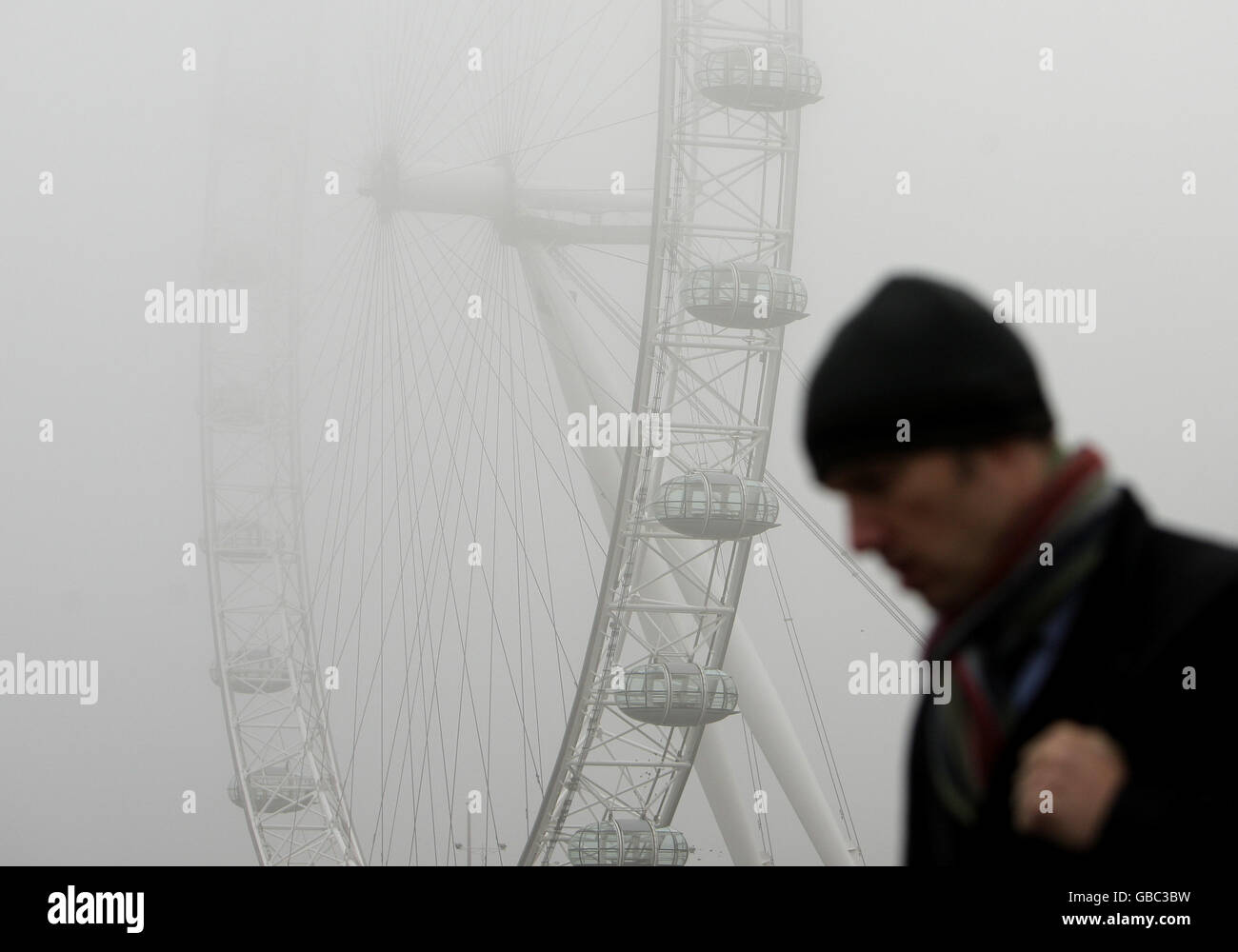 Un pedone sul Westminster Bridge, come il London Eye, sulla sponda sud del Tamigi, è avvolto dalla nebbia. Foto Stock