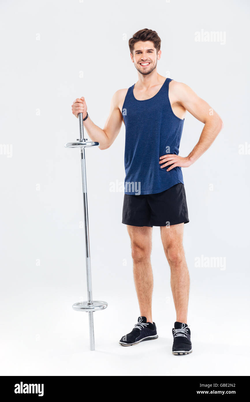 A piena lunghezza Ritratto di un felice giovane atleta in piedi con barbell isolata su uno sfondo grigio Foto Stock