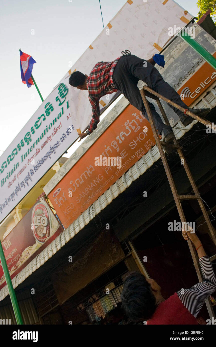 Un uomo è la scopertura di un segno che indica la posizione di una nuova scuola di lingua inglese nel villaggio di Chork, Cambogia. Foto Stock