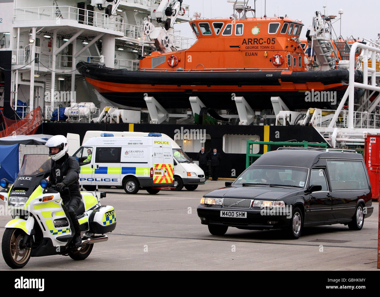 Un'udienza porta i corpi di alcuni degli uomini che sono stati uccisi quando un elicottero si è schiantato nel Mare del Nord dopo che sono stati tolti dalla nave della Vittoria Caledonica (nella foto posteriore) al porto di Aberdeen. Foto Stock