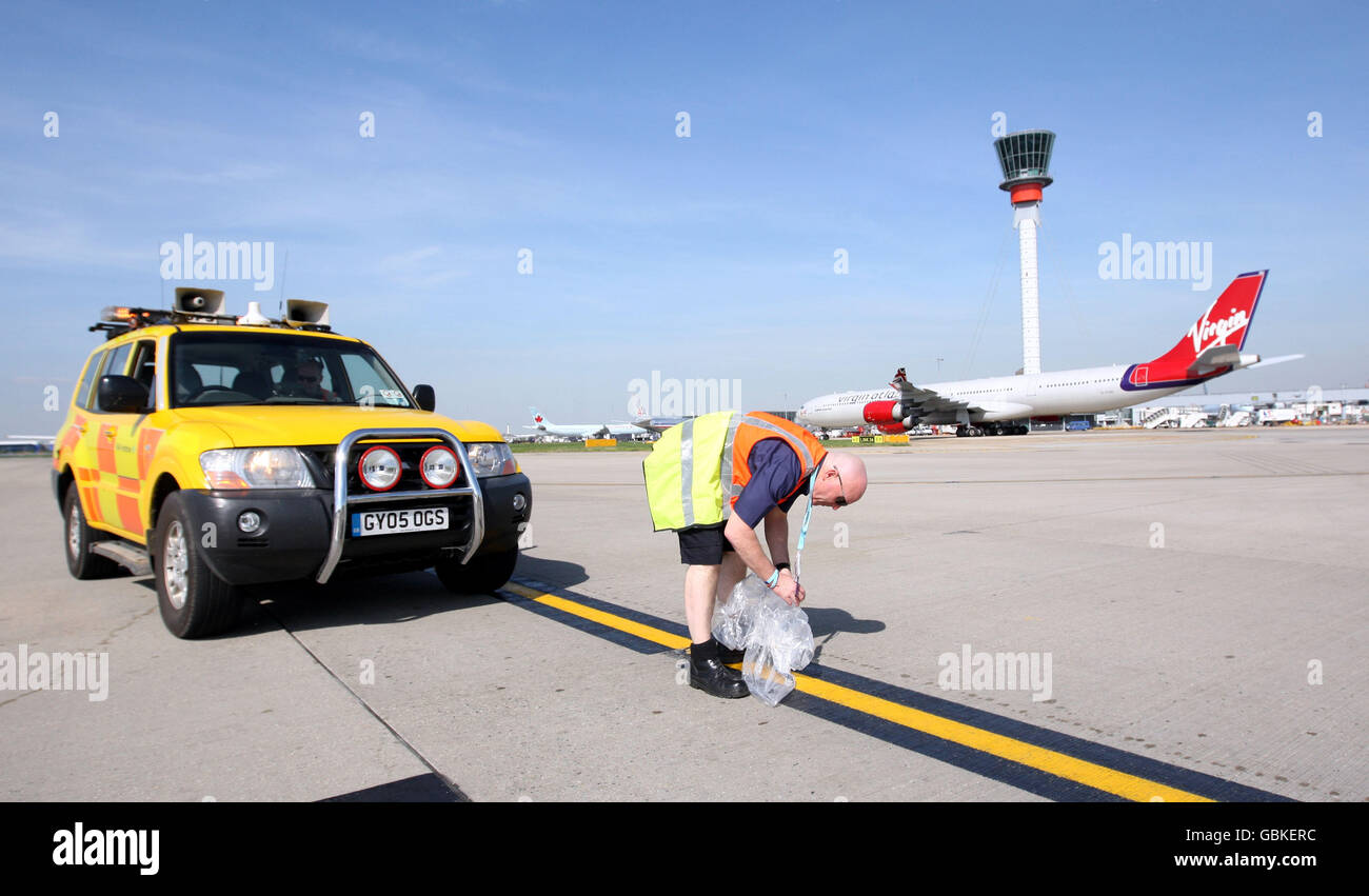 Un membro del team Airside Operations che lavora per eliminare la pista di spazzatura o detriti di oggetti estranei (FOD) all'aeroporto di Heathrow, Middlesex. Foto Stock