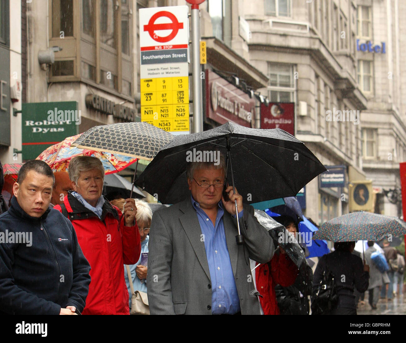 La gente si rifugia sotto gli ombrelloni mentre attendono un autobus sullo Strand nel centro di Londra, come uno sciopero di 48 ore da parte del sindacato RMT causa gravi danni alla metropolitana di Londra. Foto Stock