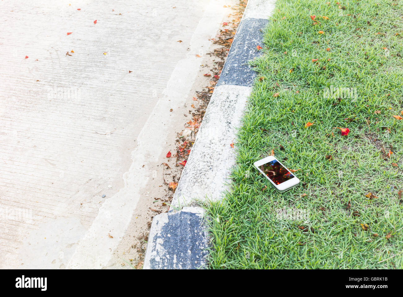 Smartphone sul campo in erba di fianco alla strada,caduta o perdita dello smartphone o cellulare o telefono cellulare su street,mancante e perdita belon Foto Stock