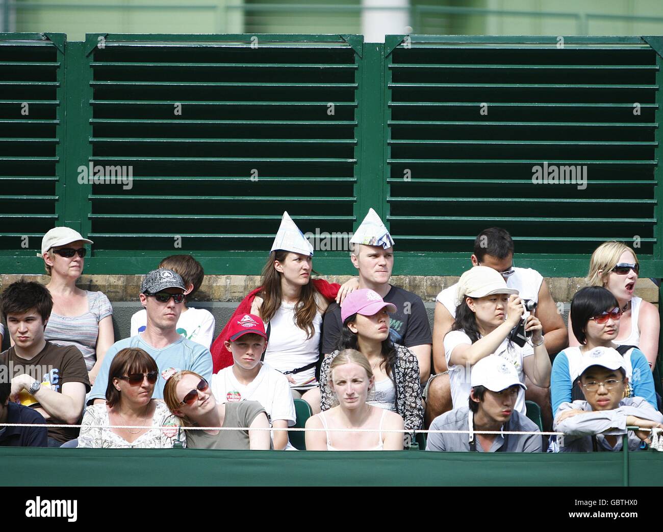 Due appassionati di tennis indossano cappelli di carta per proteggerli Il sole mentre guardano l'Agnieszka Radwanska polacca giocare contro La Cina Na li d durante i Campionati di Wimbledon 2009 a. All England Tennis Club Foto Stock