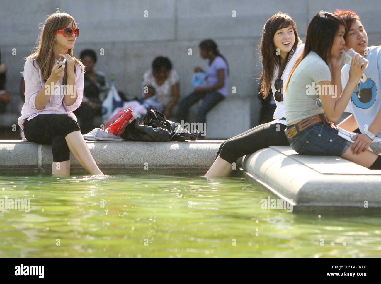 La gente siede sul bordo di una fontana in Trafalgar Square, nel centro di Londra, che ha acqua verde a causa di un accumulo di alghe. Foto Stock