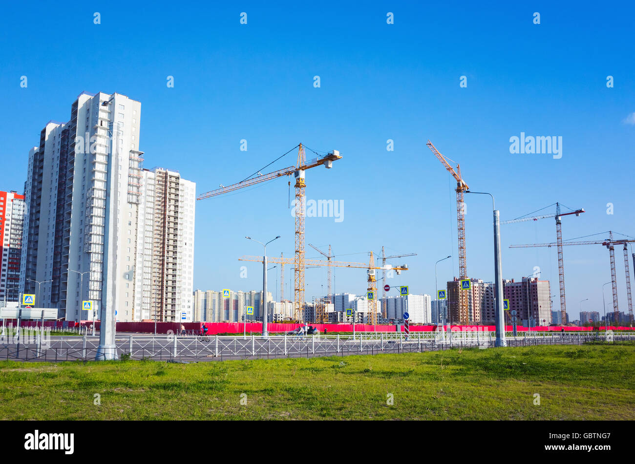 Blocco di appartamenti in costruzione, lavorando gru sono sotto il cielo blu nel giorno di estate Foto Stock