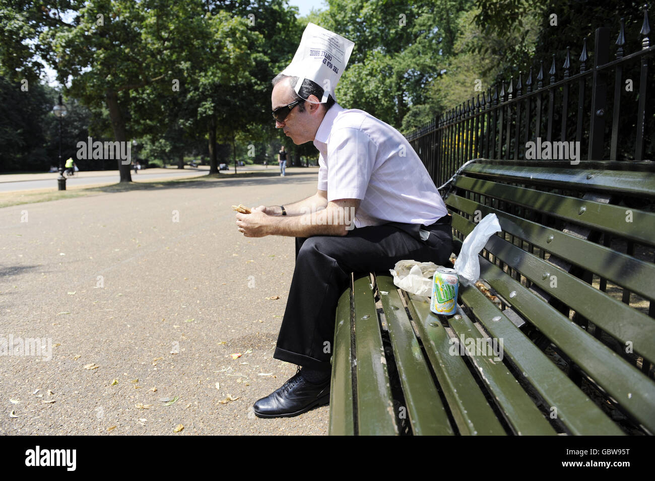 Un lavoratore in ufficio durante la pausa pranzo a Hyde Park di Londra, cerca di tenere il sole dalla testa utilizzando una borsa sandwich come cappello durante il tempo caldo. Foto Stock