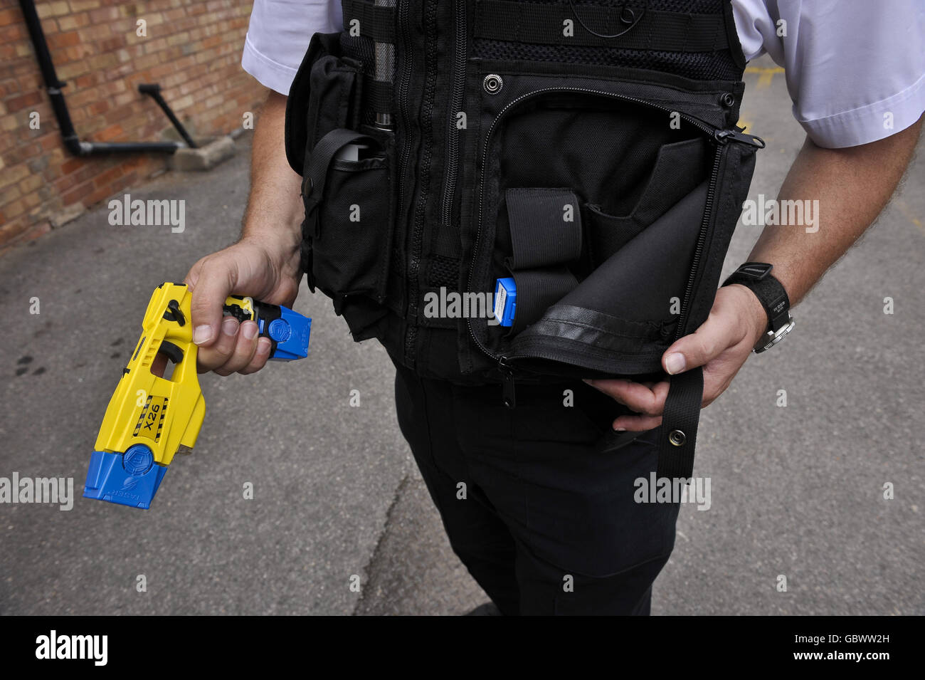 Un poliziotto tiene un Taser X26 in una mano dotato di cartucce blu per l'allenamento e mostra la custodia dove la pistola è stata inserita Foto Stock