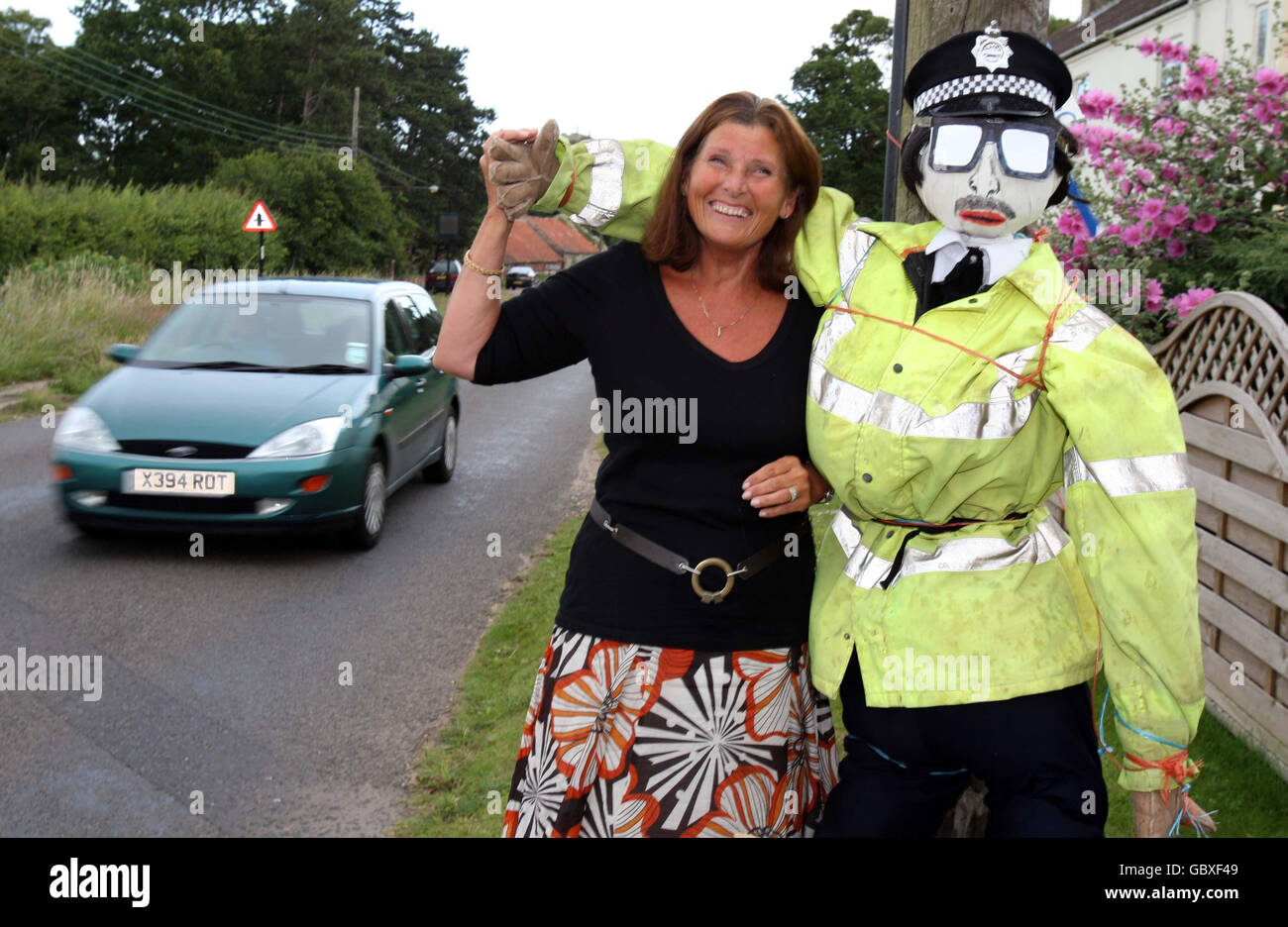 Miranda Skillings, azienda produttrice di scaventapasseri di Brancaster Norfolk, si erge accanto al suo carrofa vestito da ufficiale del traffico all'ingresso del villaggio di Brancaster, a Norfolk. Foto Stock